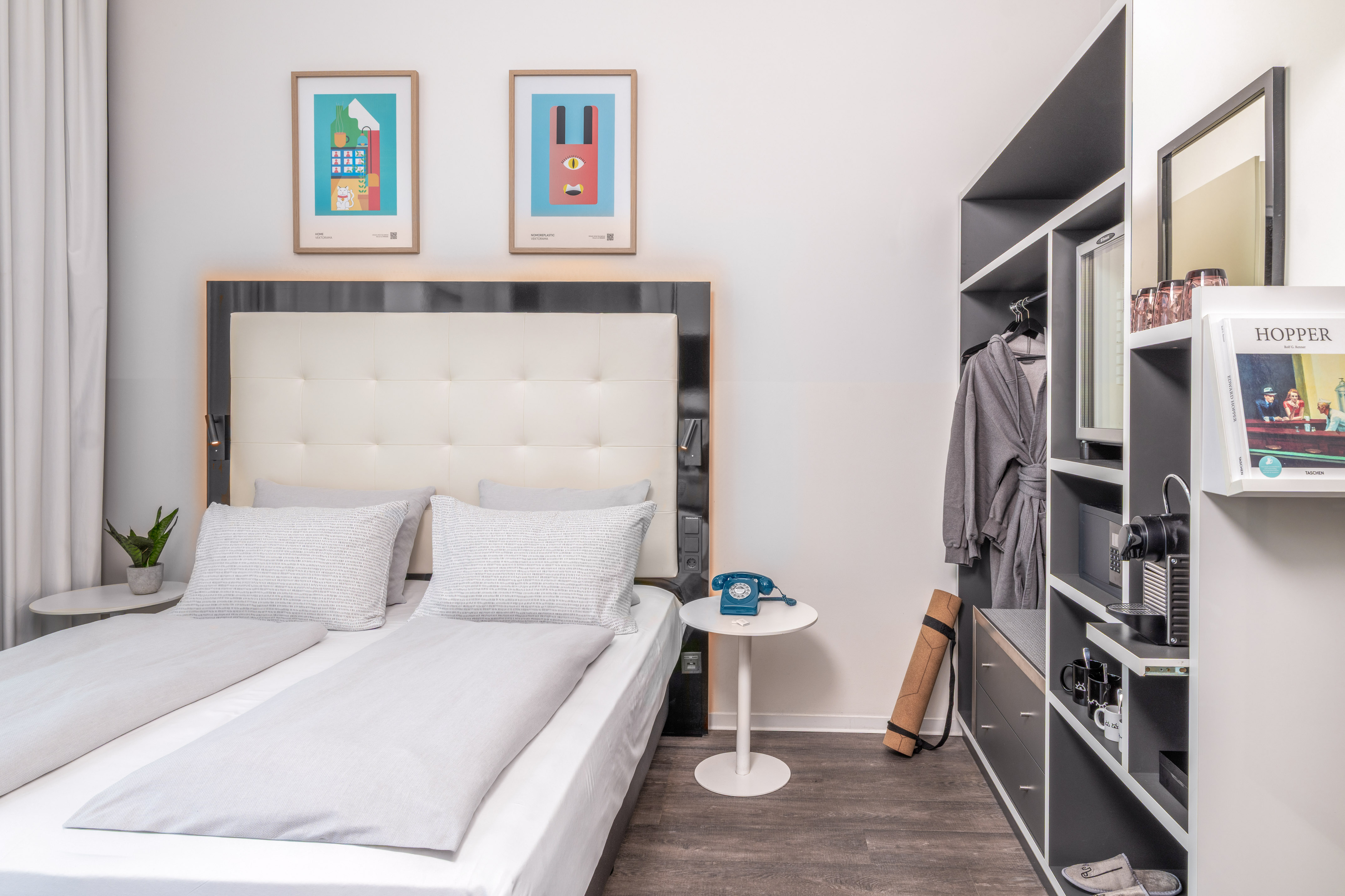 Modern hotel bedroom with light grey bed, colorful art, and built-in closet.