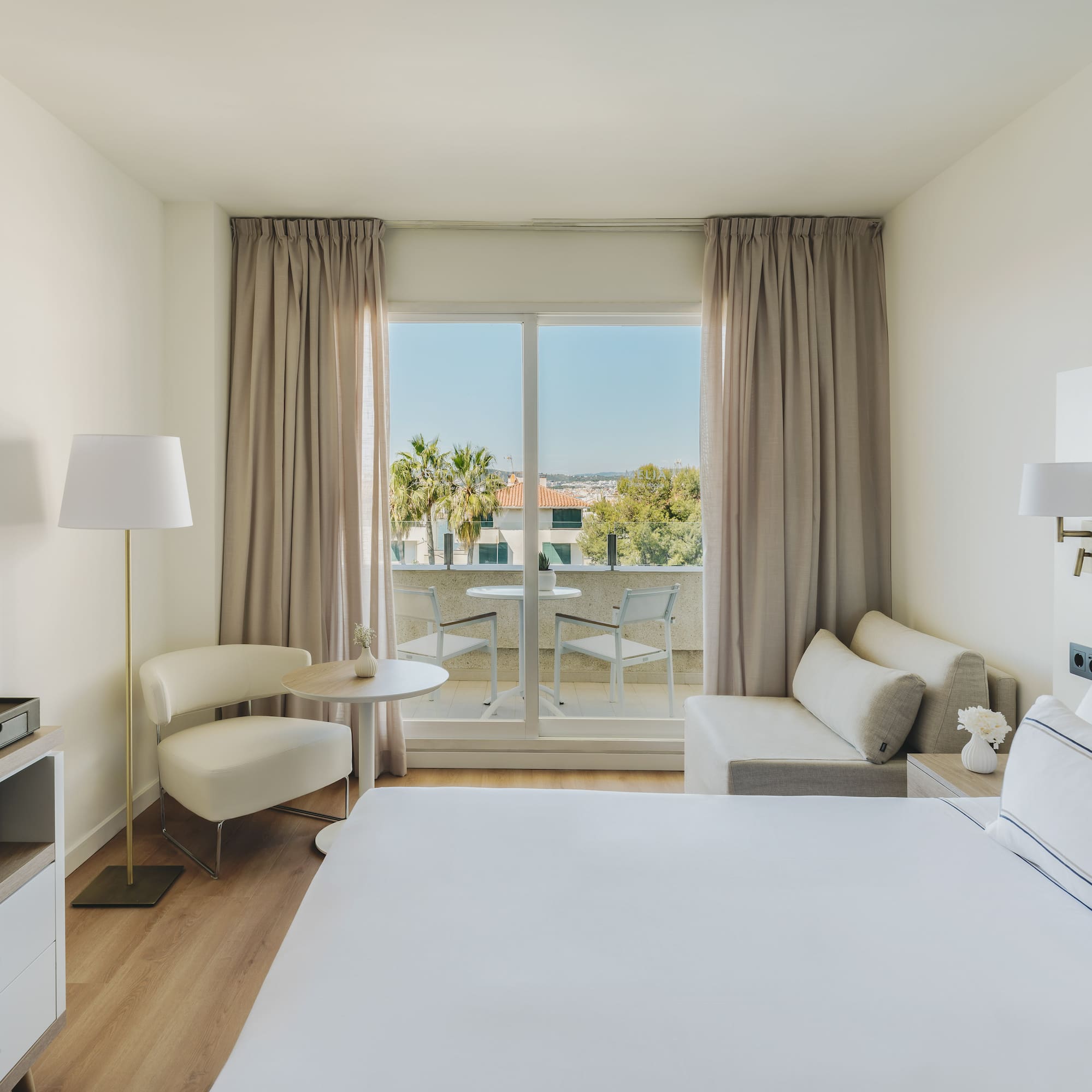 Habitación de hotel moderna con balcón, cama, sofá y vistas al exterior.