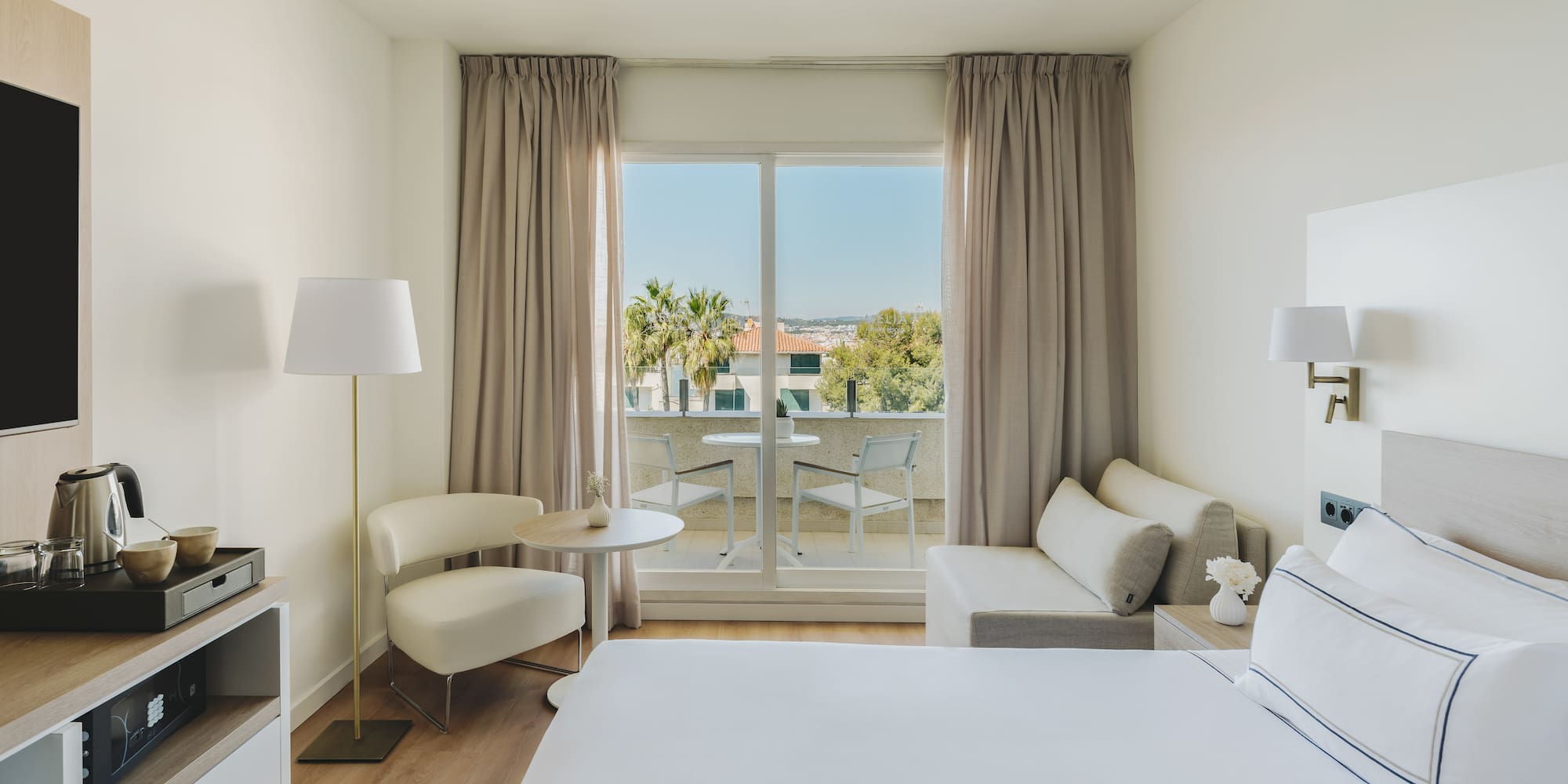 Habitación de hotel moderna con balcón, cama, sofá y vistas al exterior.