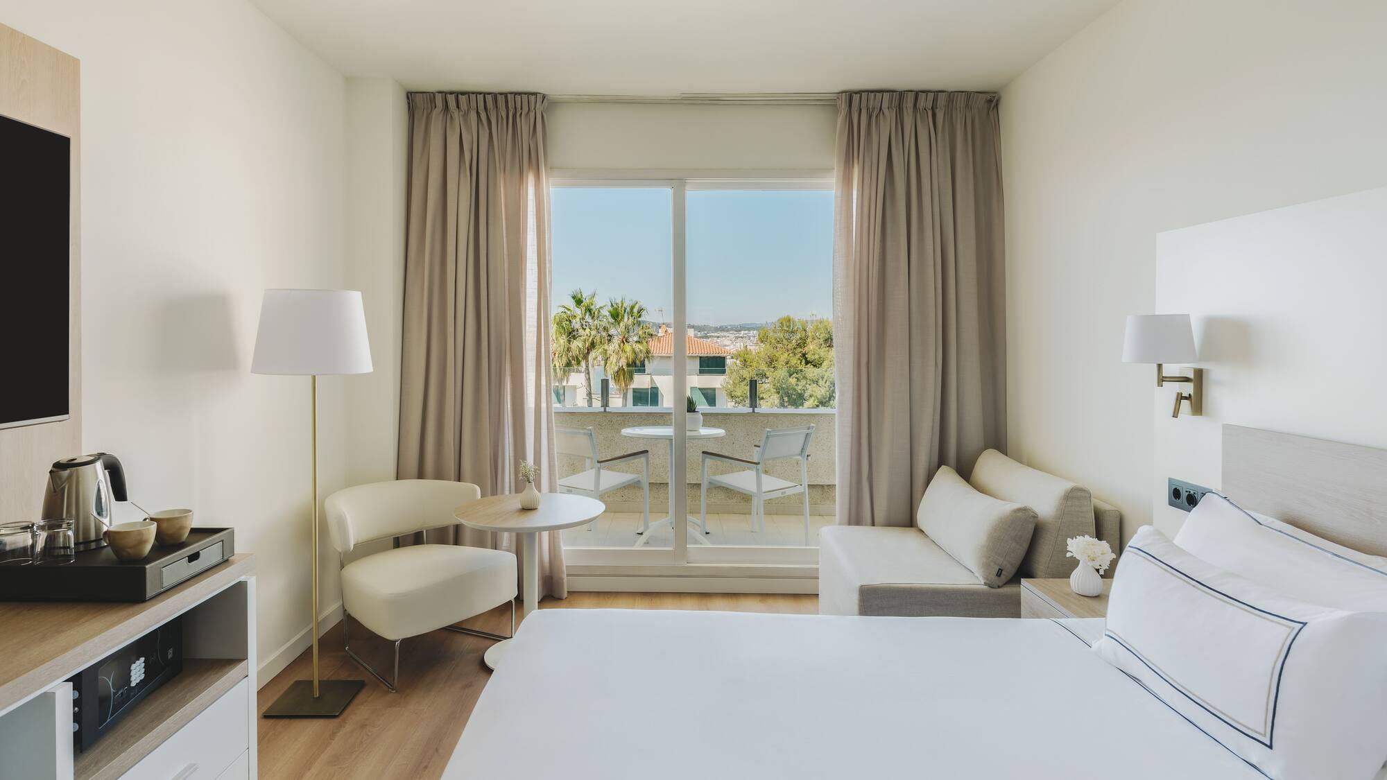Habitación de hotel moderna con balcón, cama, sofá y vistas al exterior.