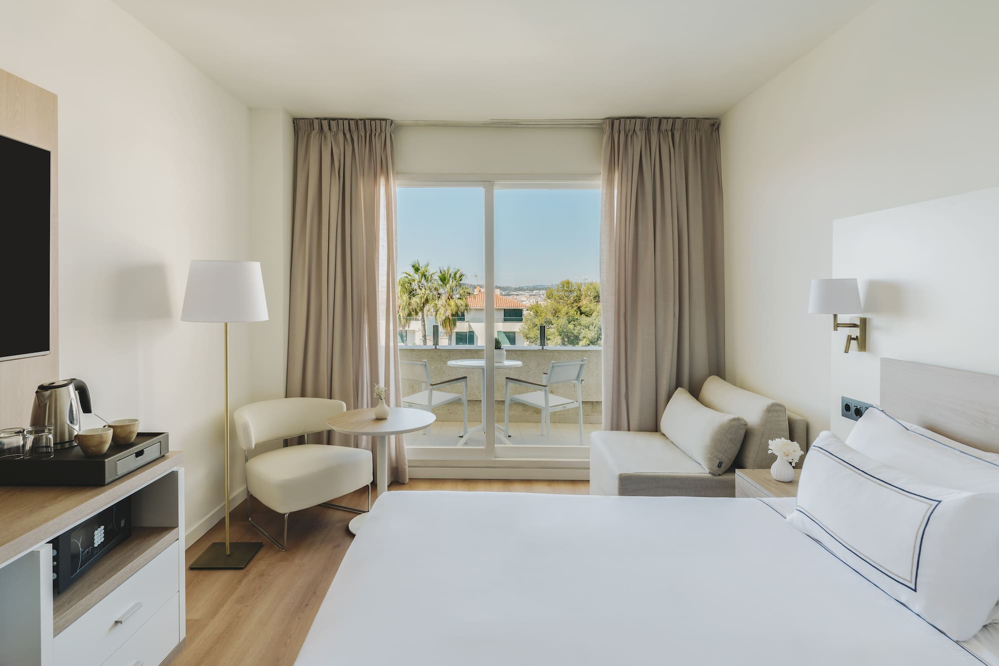 Habitación de hotel moderna con balcón, cama, sofá y vistas al exterior.