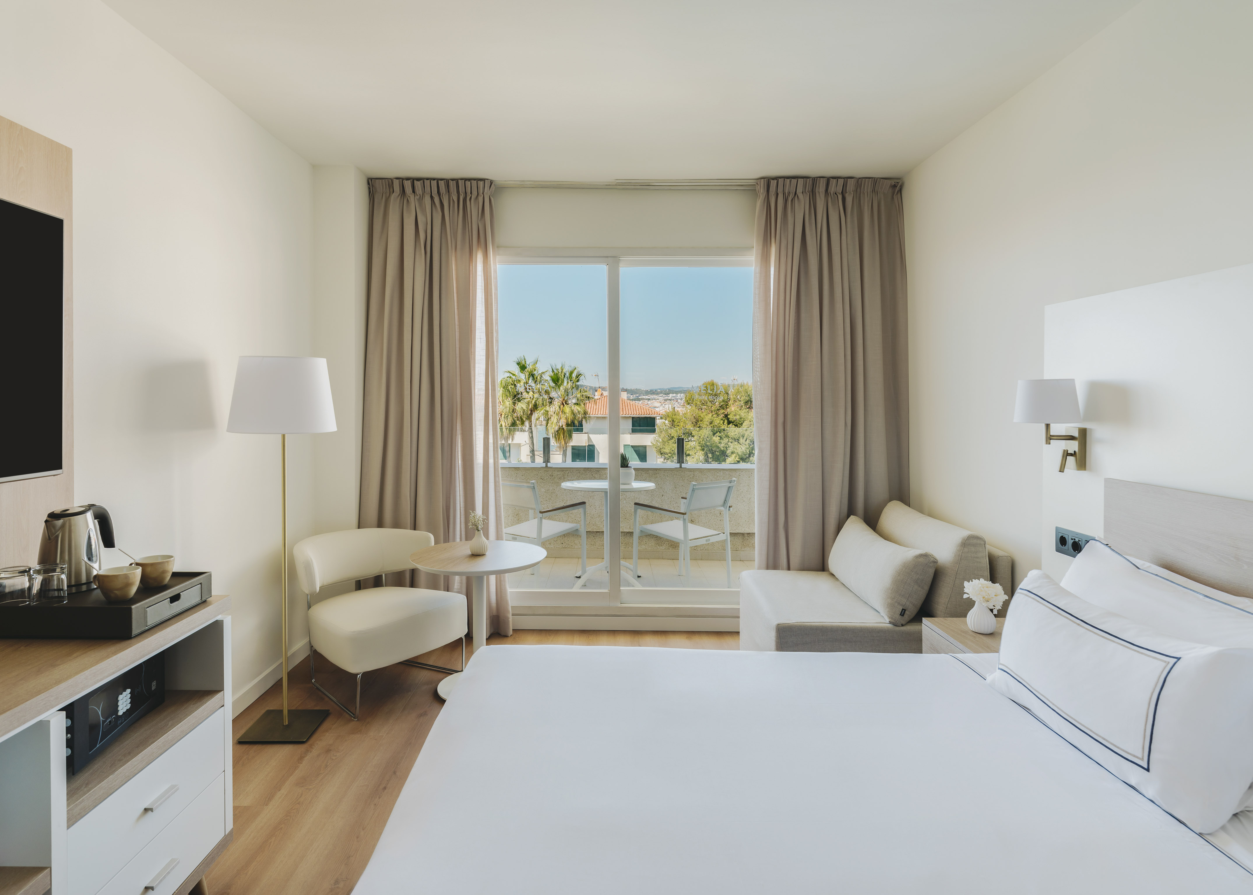 Habitación de hotel moderna con balcón, cama, sofá y vistas al exterior.