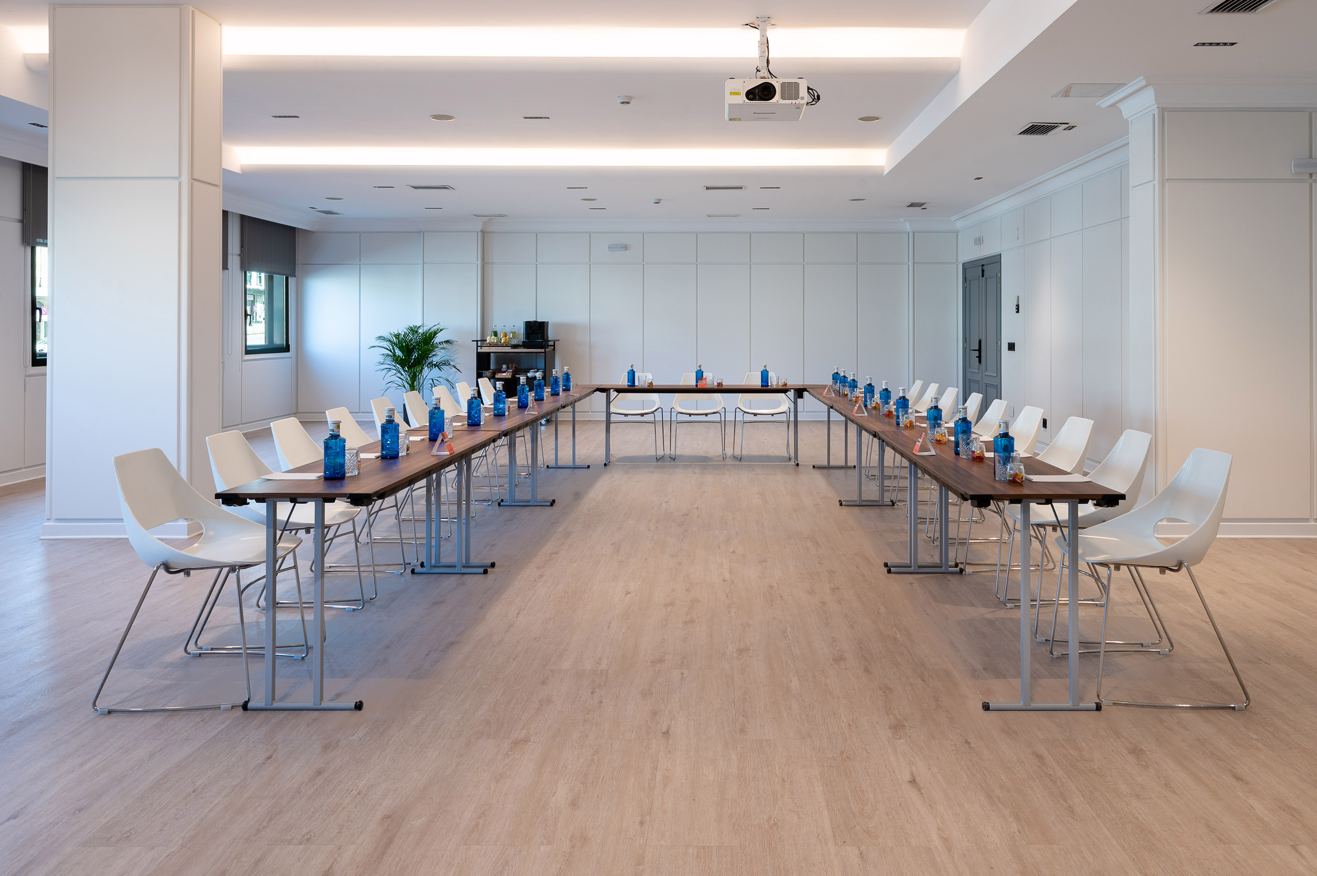 Modern U-shaped conference room setup with white chairs and ceiling projector.