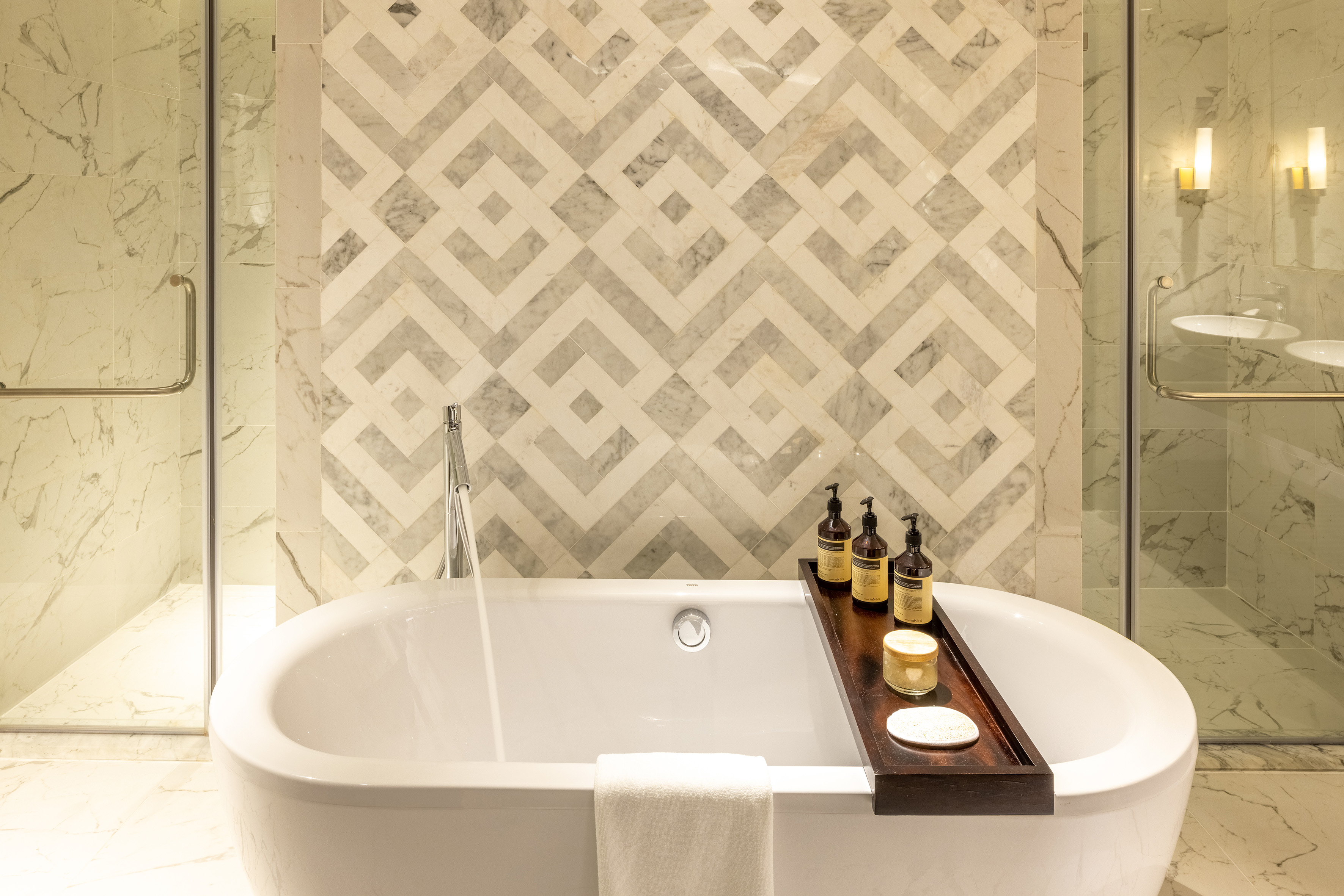 Modern luxury bathroom with freestanding tub, geometric marble wall, and toiletries.