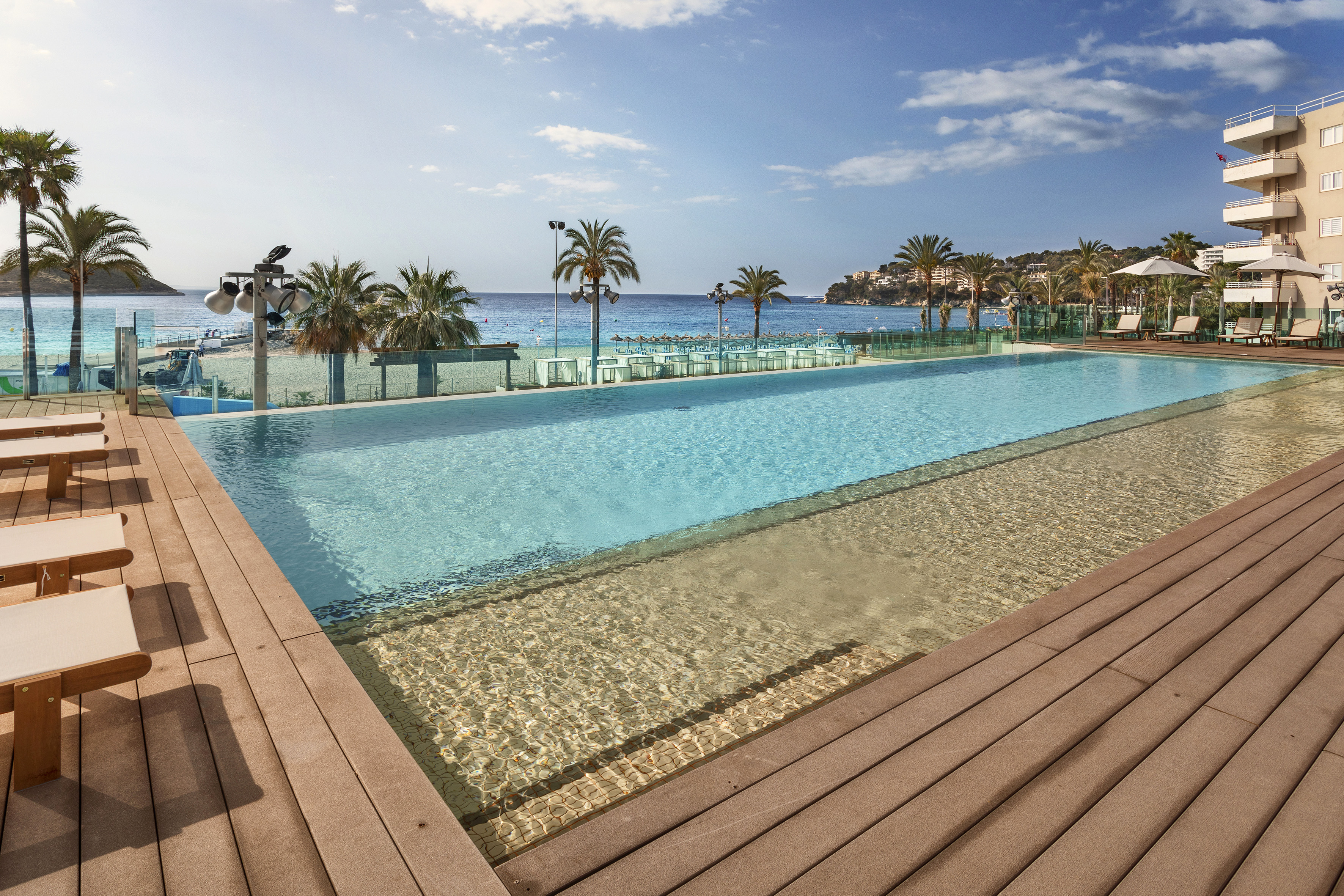 Resort infinity pool with ocean view, sandy beach, palm trees, and hotel.