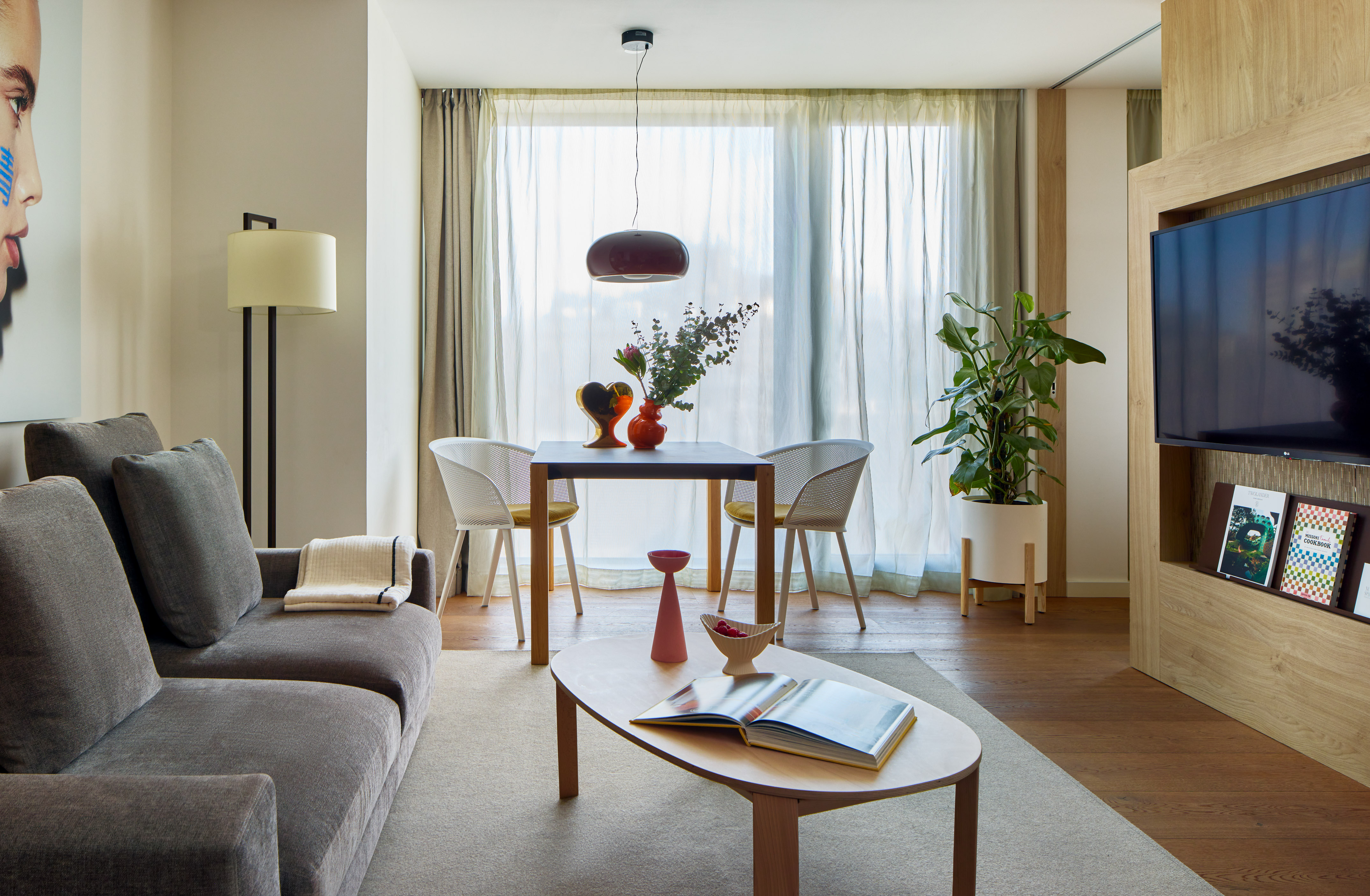 Modern hotel suite living area with sofa, dining set, and large window.