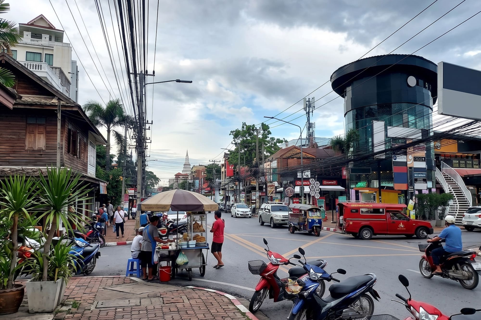 Bustling Southeast Asian street scene with food stall, motorbikes, and traffic.