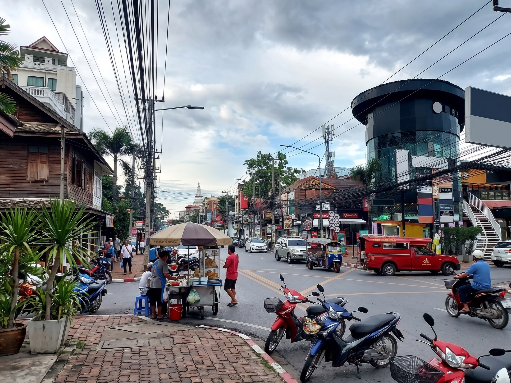 Bustling Southeast Asian street scene with food stall, motorbikes, and traffic.