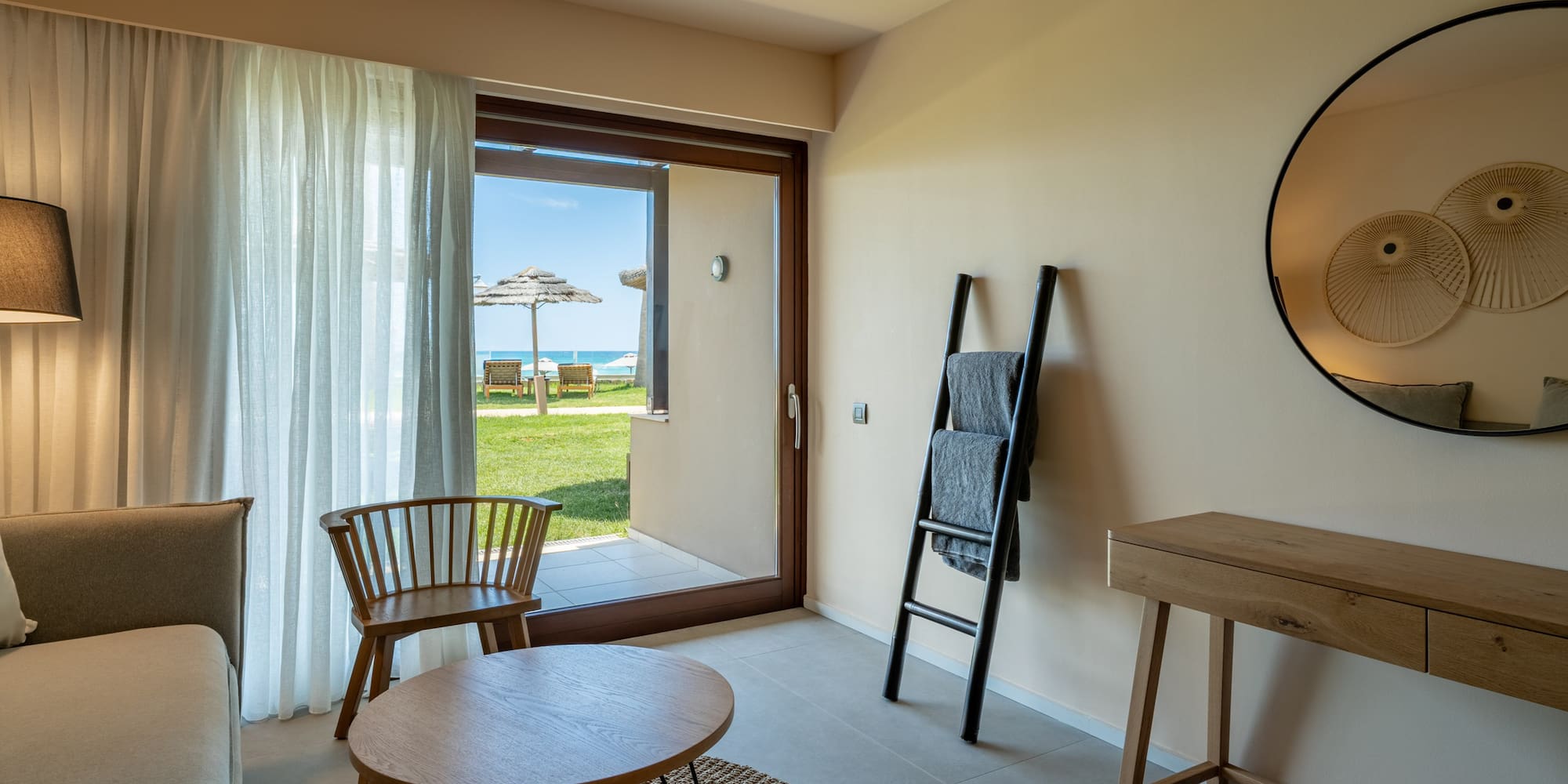 Modern hotel room with beach view patio, sofa, and contemporary decor.