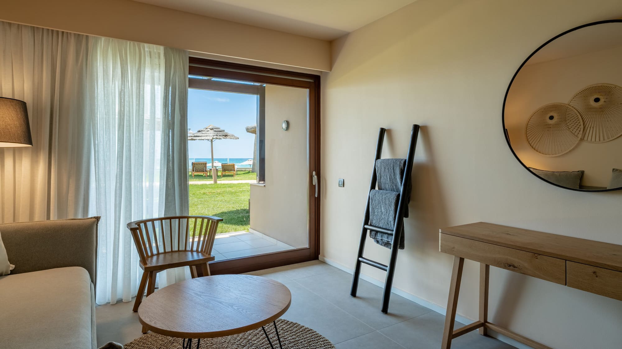 Modern hotel room with beach view patio, sofa, and contemporary decor.