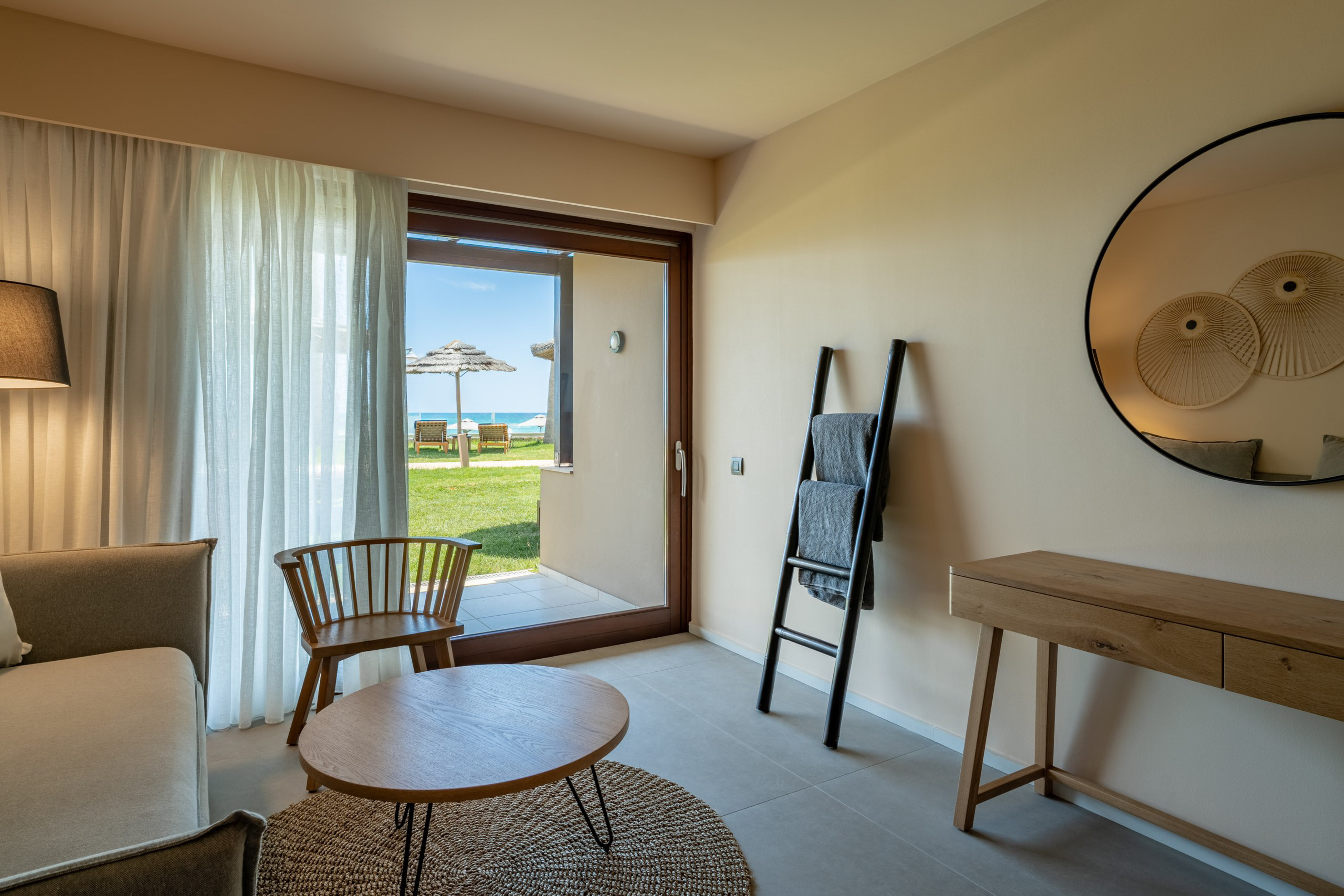 Modern hotel room with beach view patio, sofa, and contemporary decor.