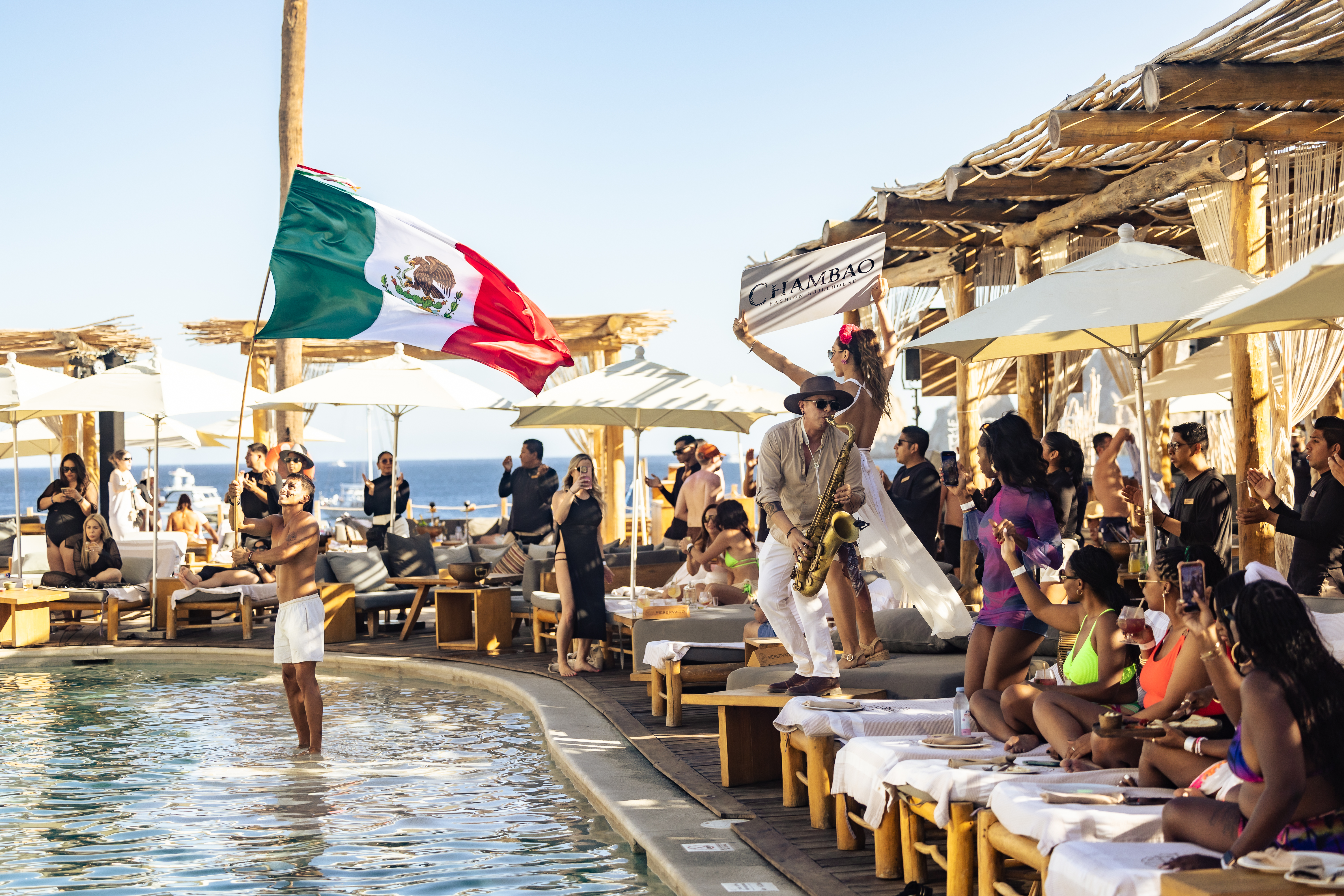 Lively pool party at a Mexican luxury beach club, saxophonist and flag.