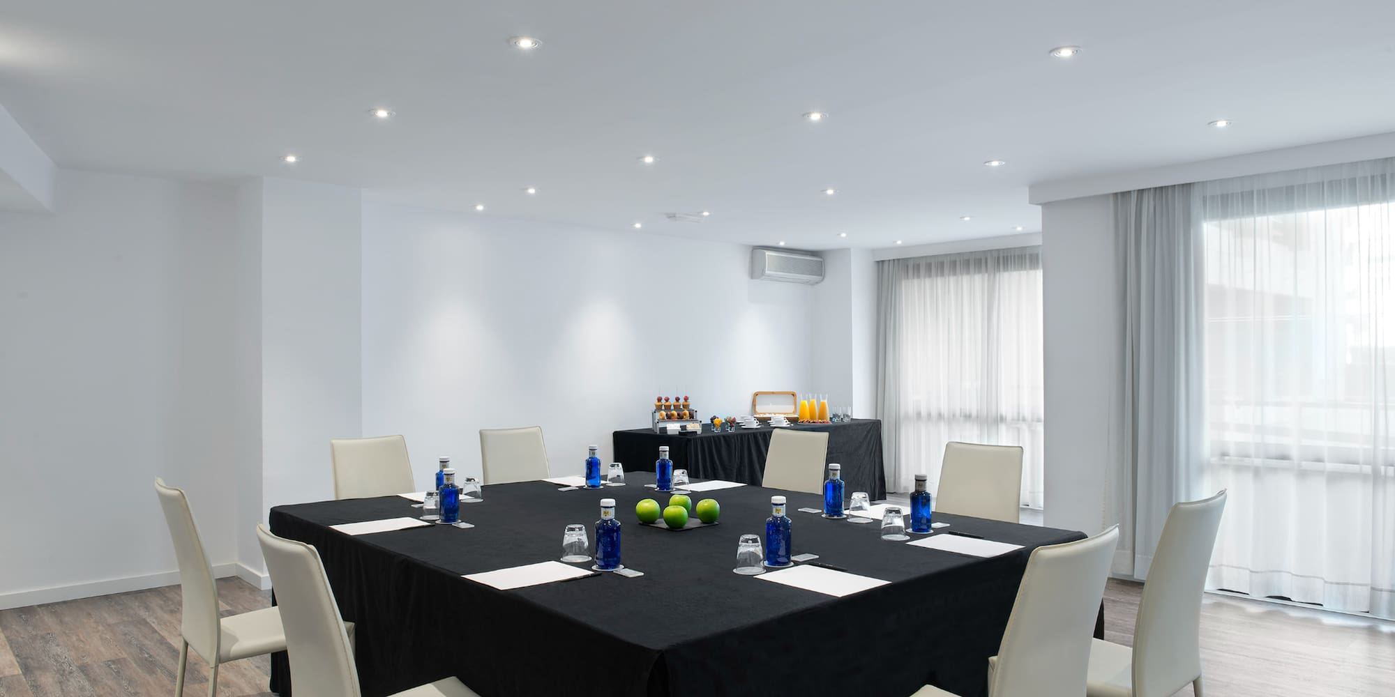 Modern meeting room with square table, white chairs, and buffet setup.