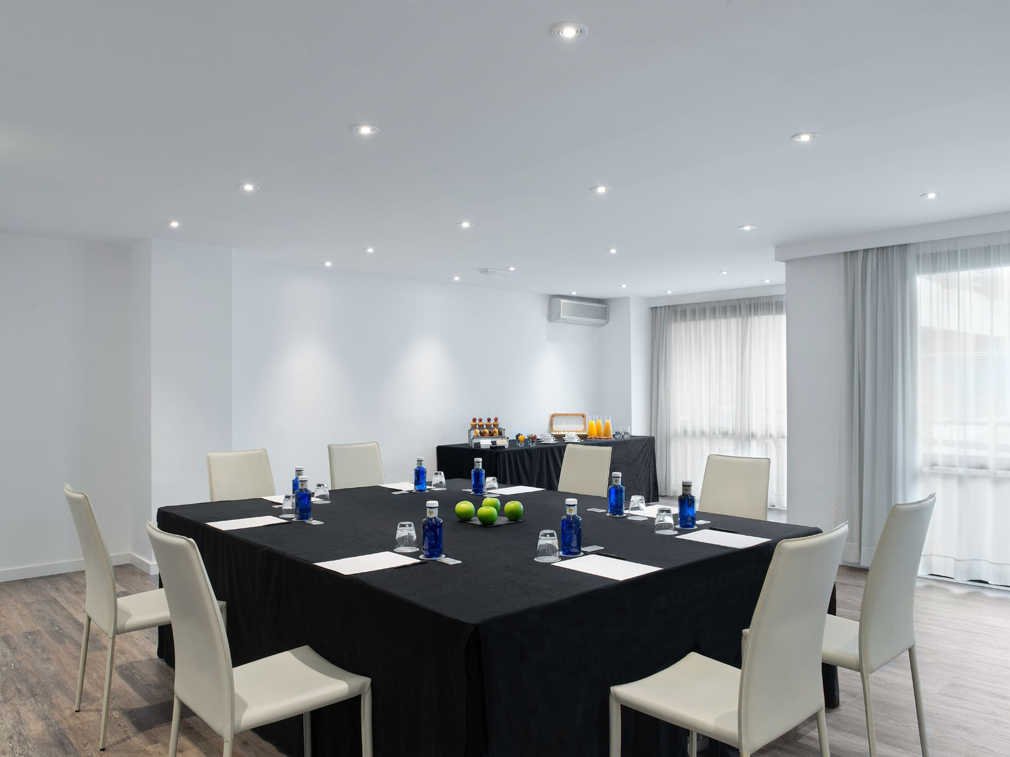 Clean conference room with square table, chairs, bottled water, and buffet.