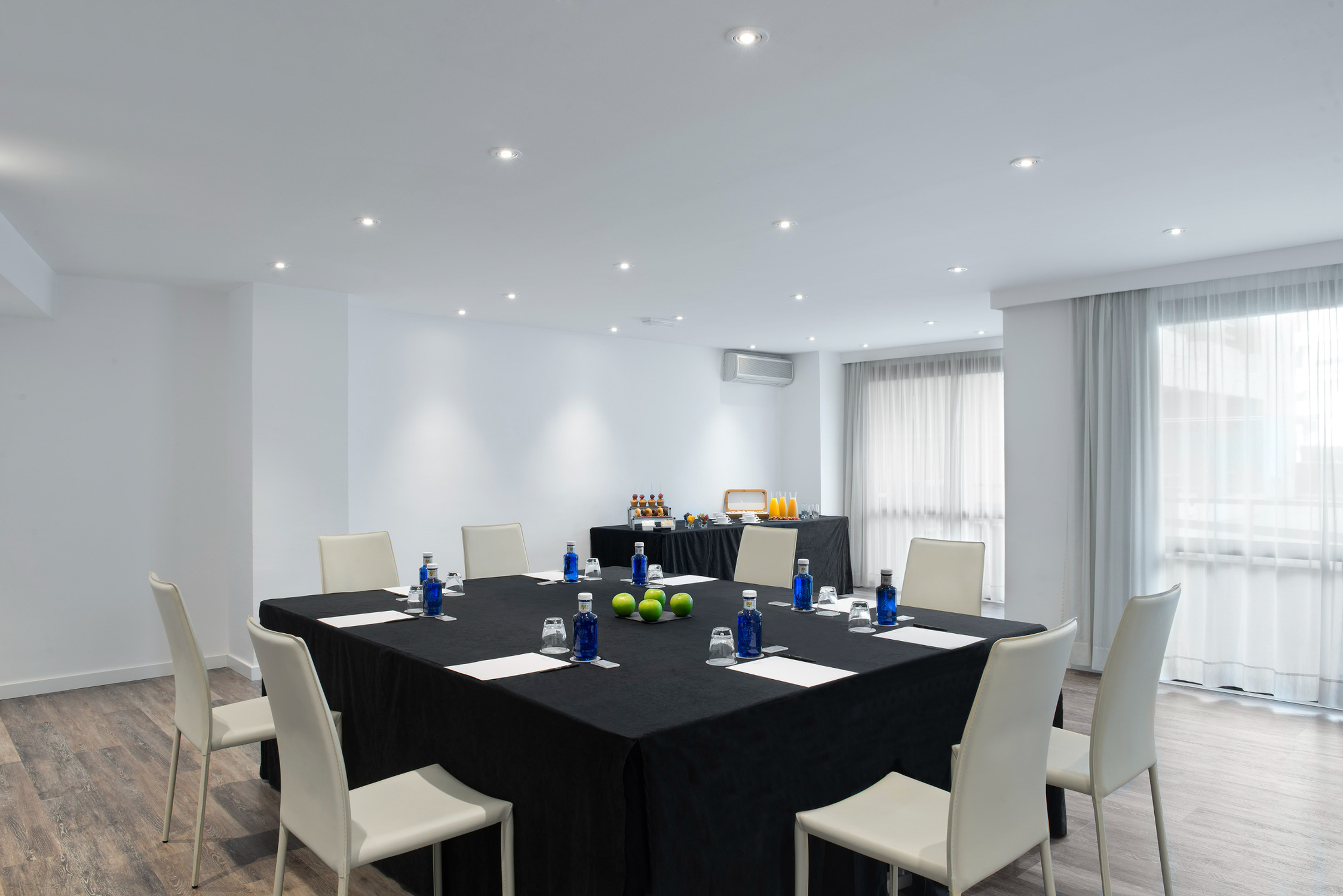 Modern meeting room with square table, white chairs, and buffet setup.