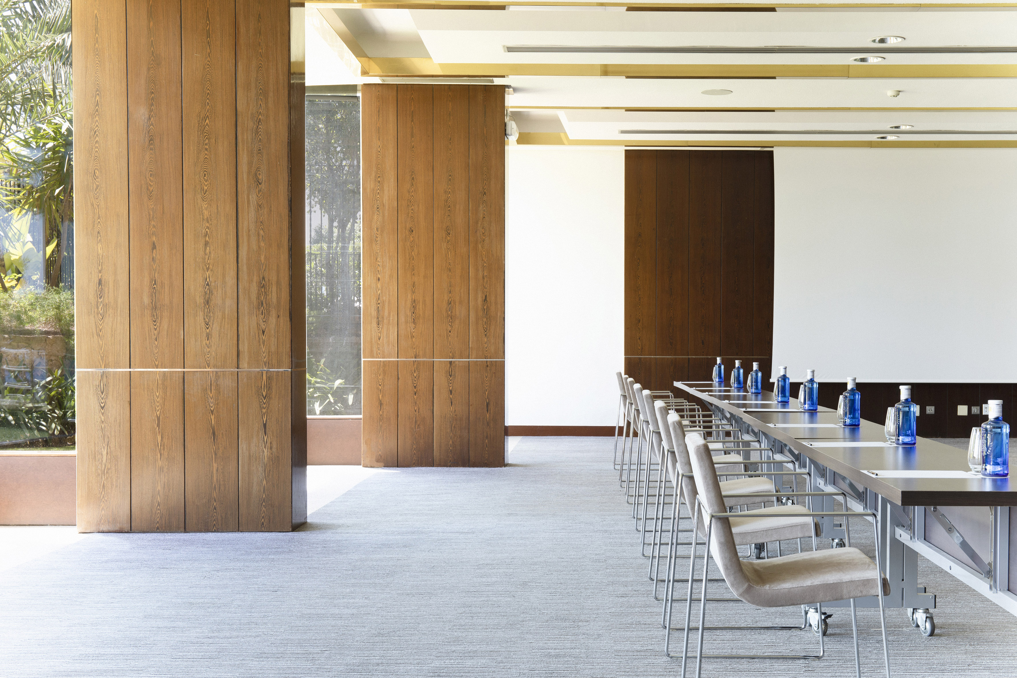 Modern conference room with long table, chairs, screen, wood paneling.