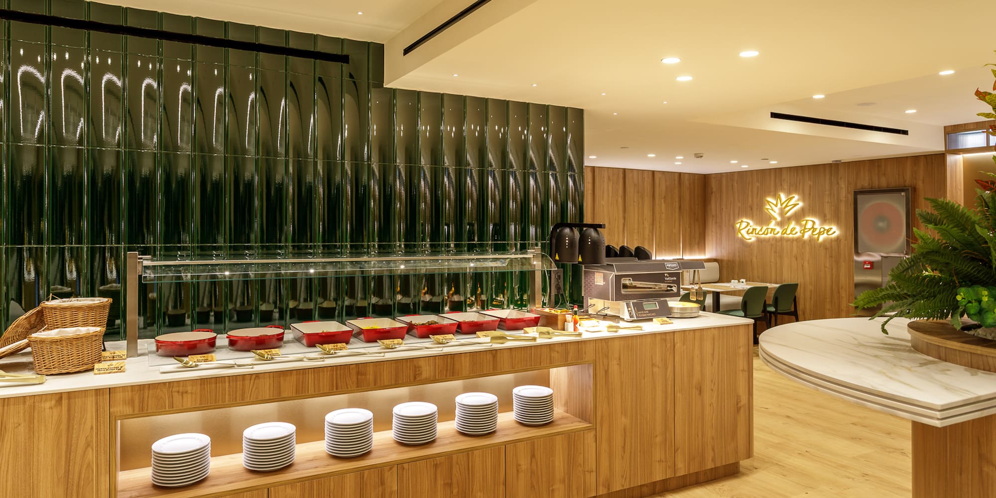 Buffet counter with food warmers, white plates, and green tiled wall in dining area.
