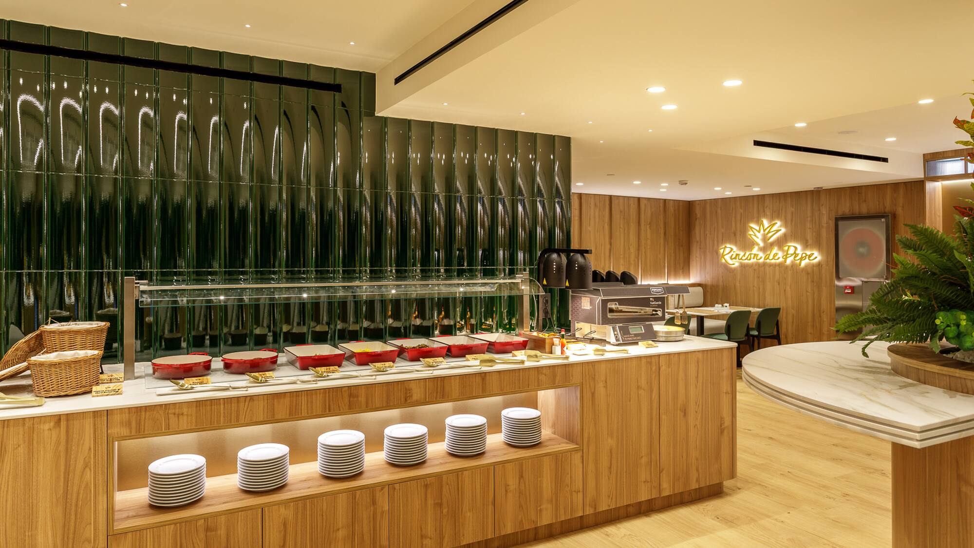 Buffet counter with food warmers, white plates, and green tiled wall in dining area.