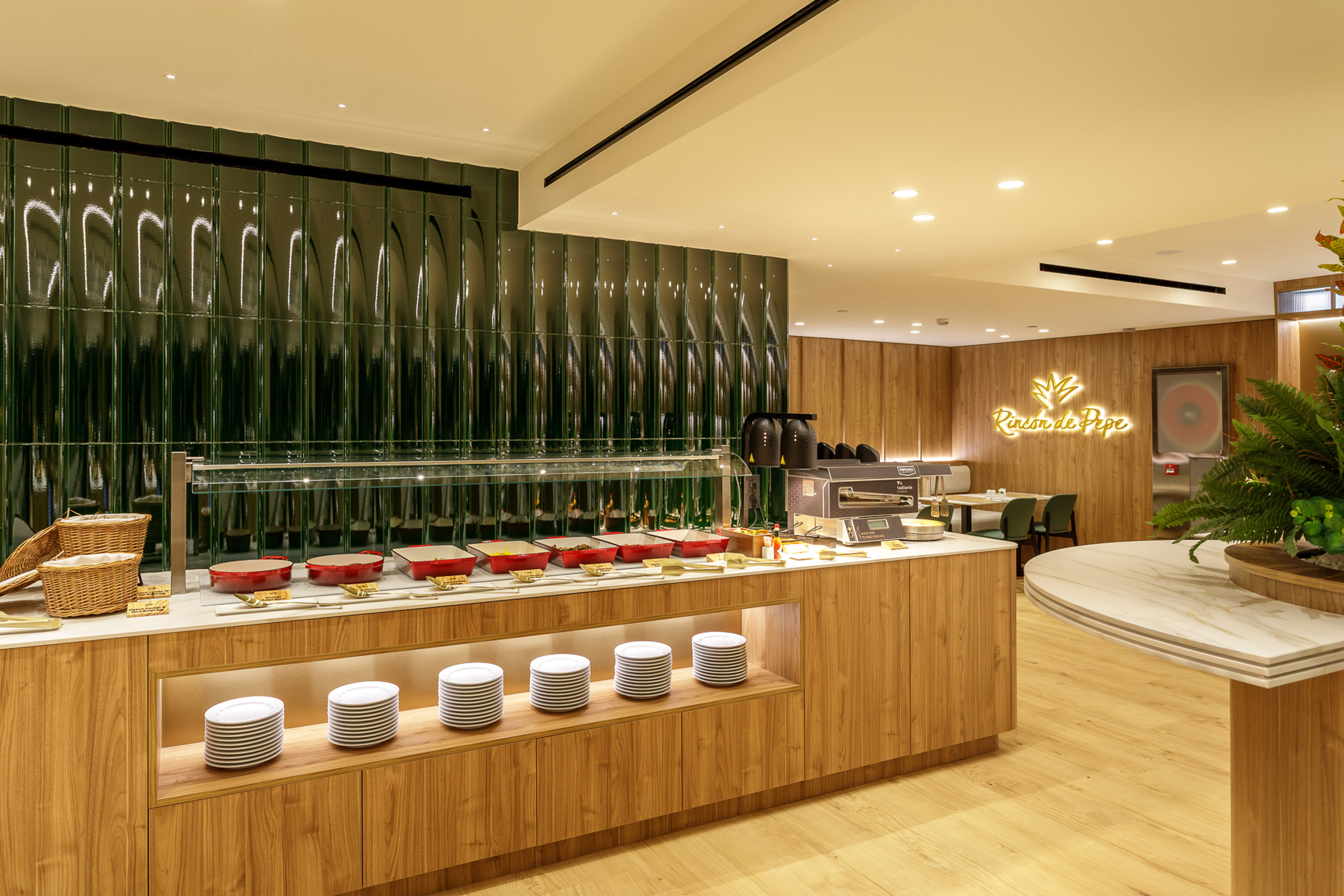 Buffet counter with food warmers, white plates, and green tiled wall in dining area.
