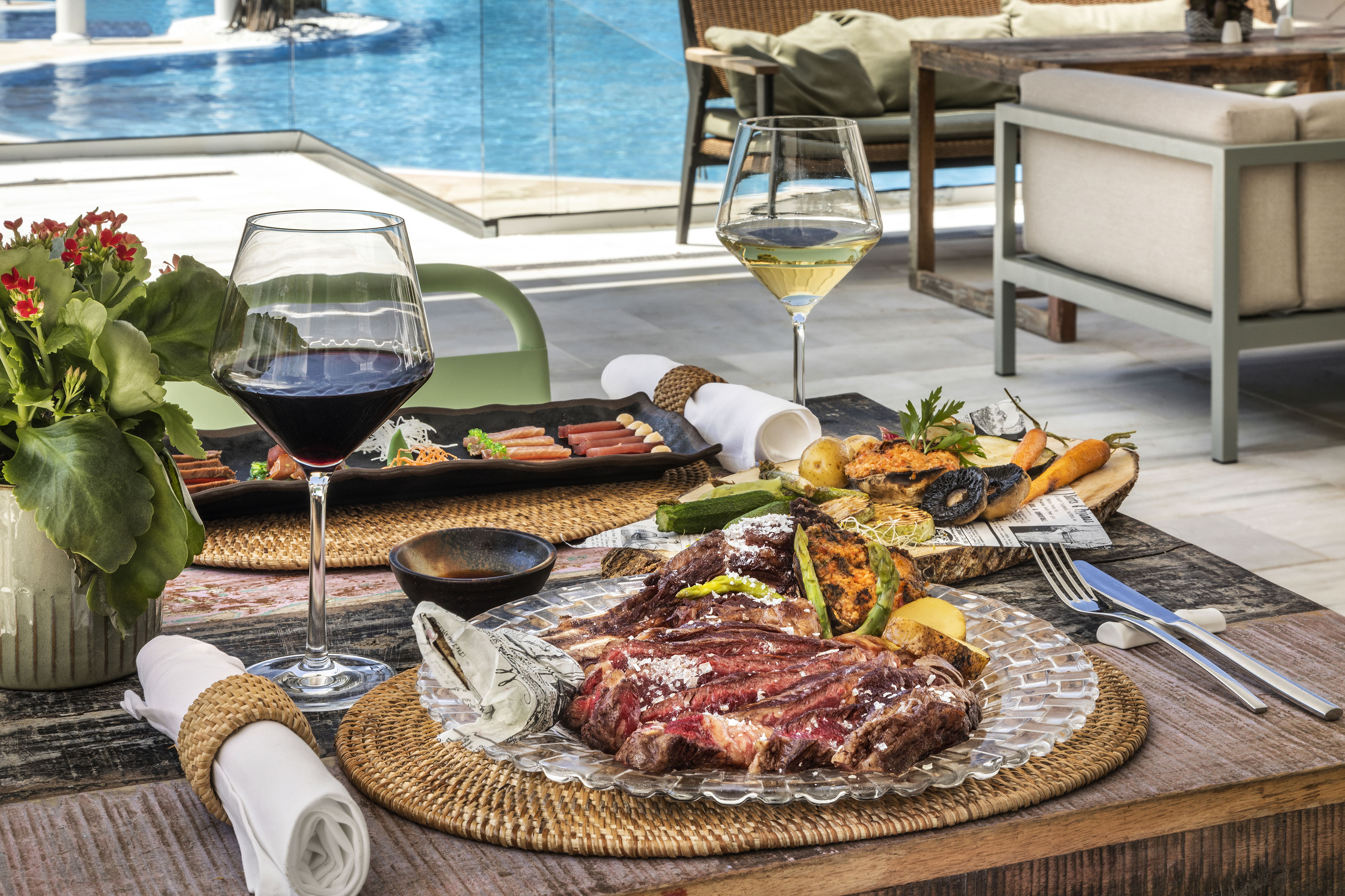 Gourmet poolside dining: sliced steak, grilled vegetables, and wine.