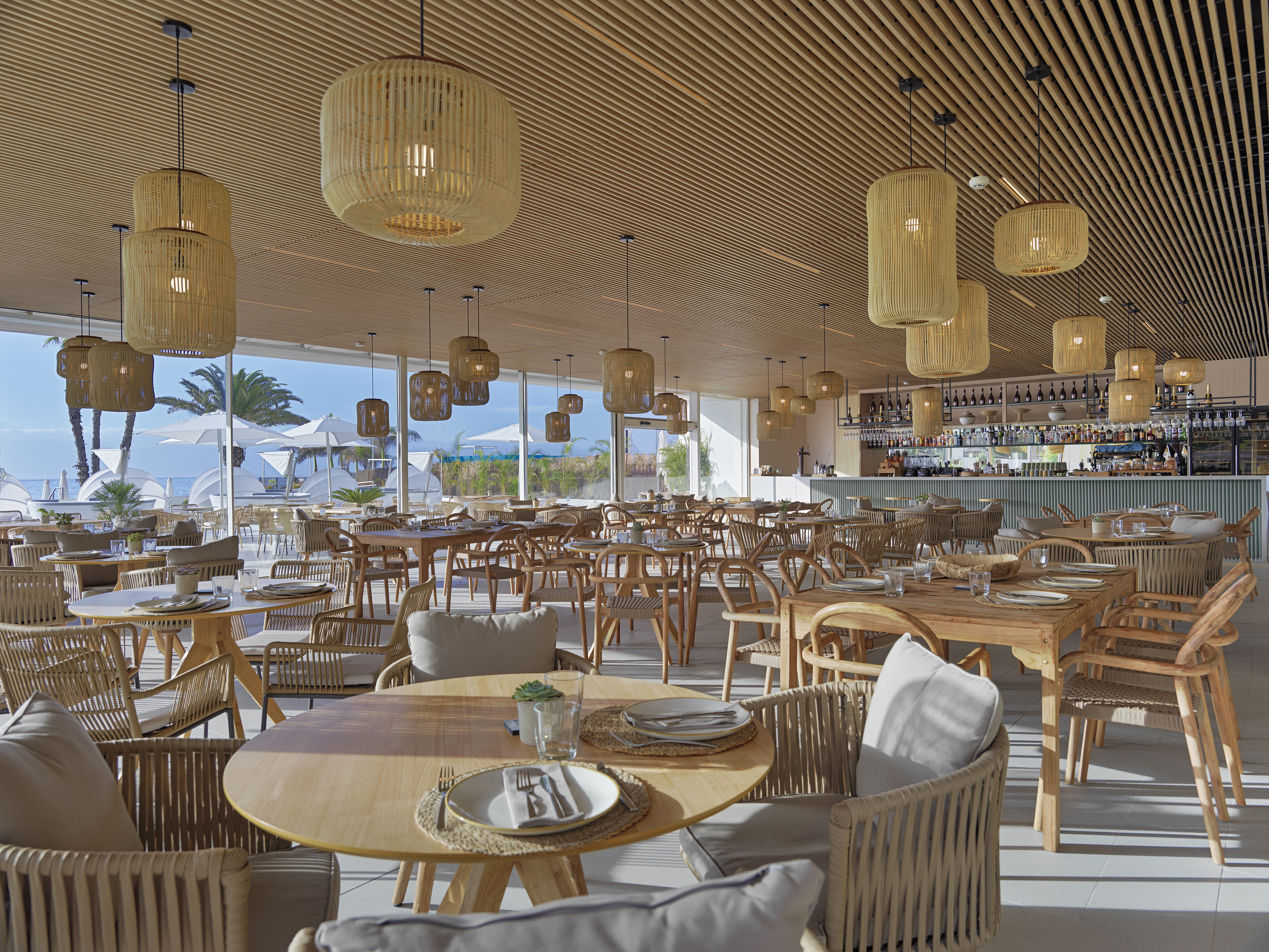 Coastal restaurant with wooden tables, wicker lights, and ocean view.