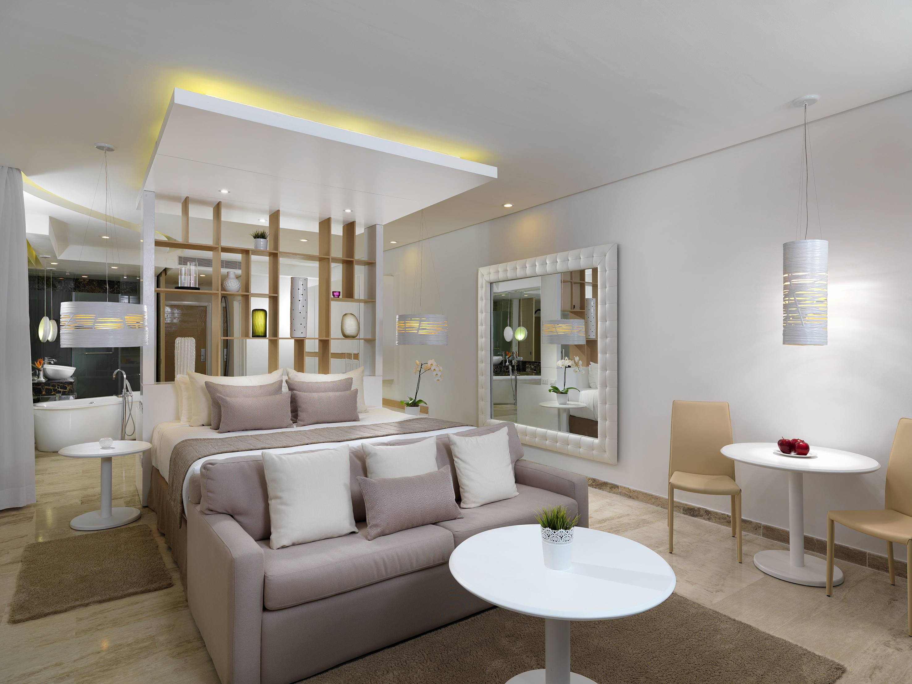 Modern open-plan hotel suite with bed, sofa, and integrated bathroom.