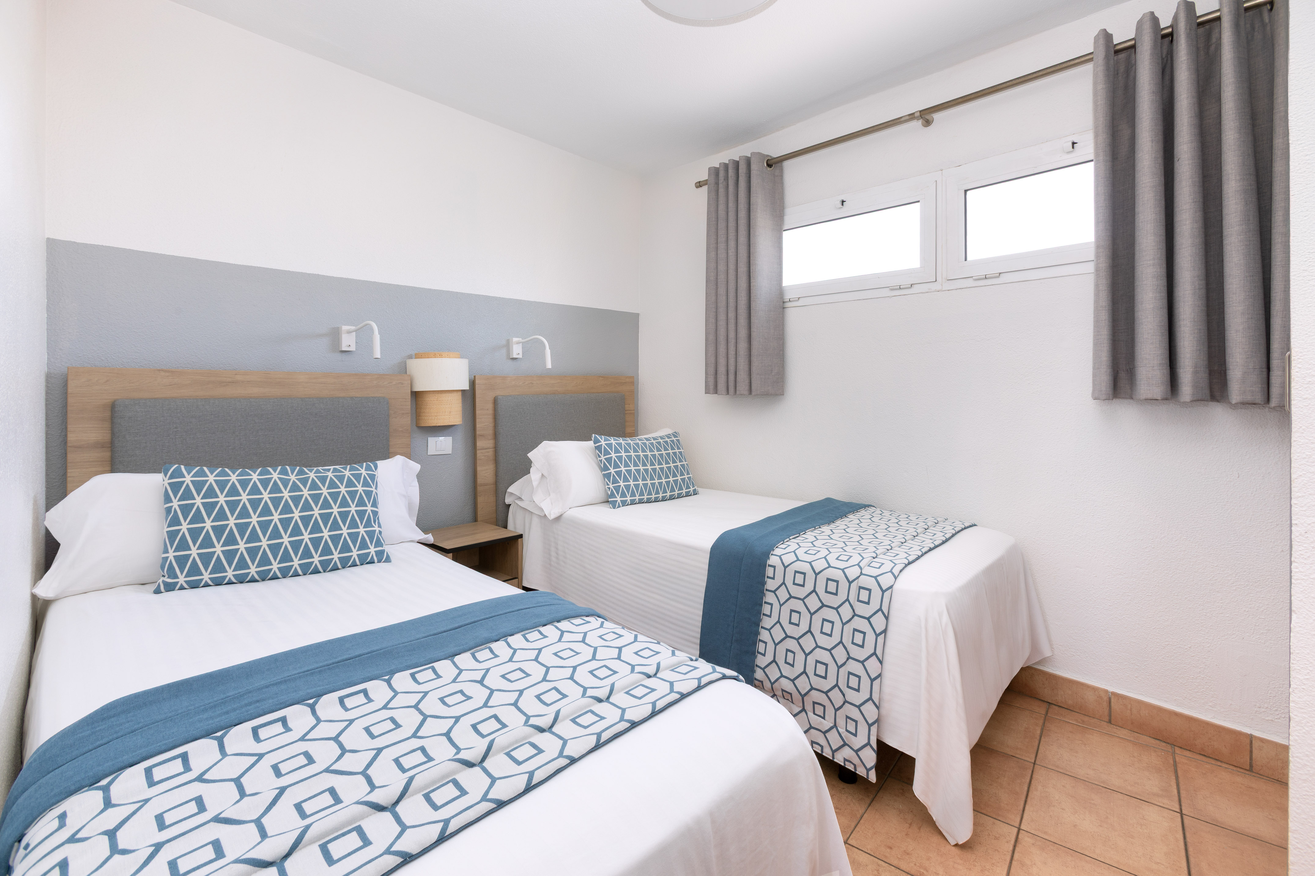 Modern hotel twin bedroom with blue geometric bedding, wood headboards.