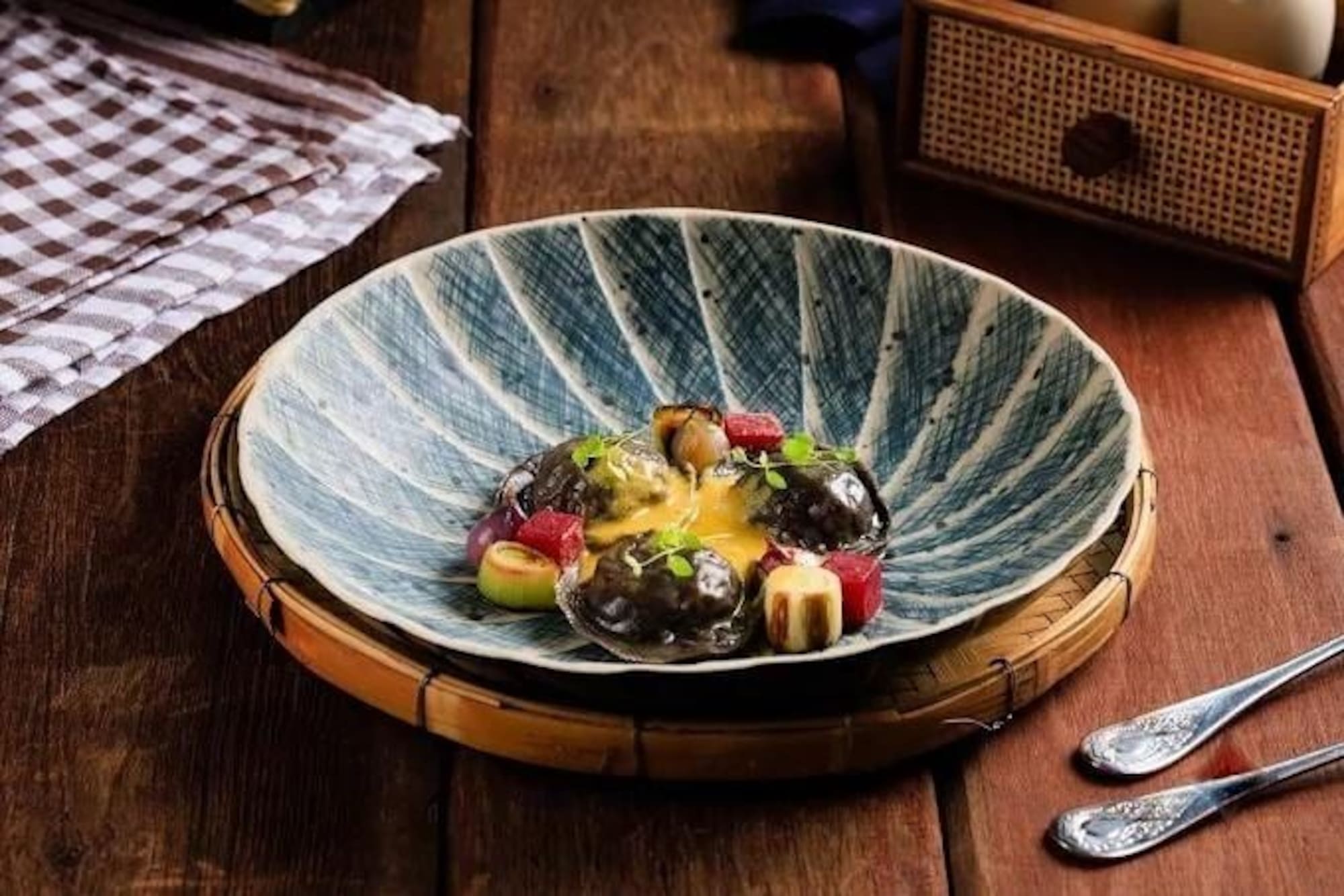 Abalone dish with yellow sauce, colorful garnishes in a patterned blue bowl on wood.