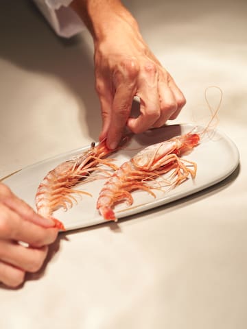 a person's hands holding a shrimp on a plate