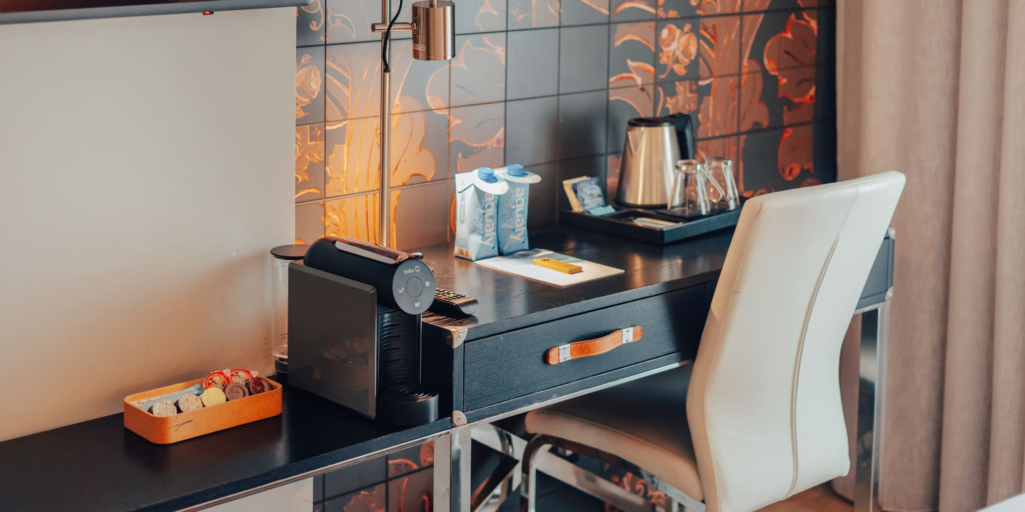 Hotel room desk featuring Nespresso machine, electric kettle, and patterned wall.