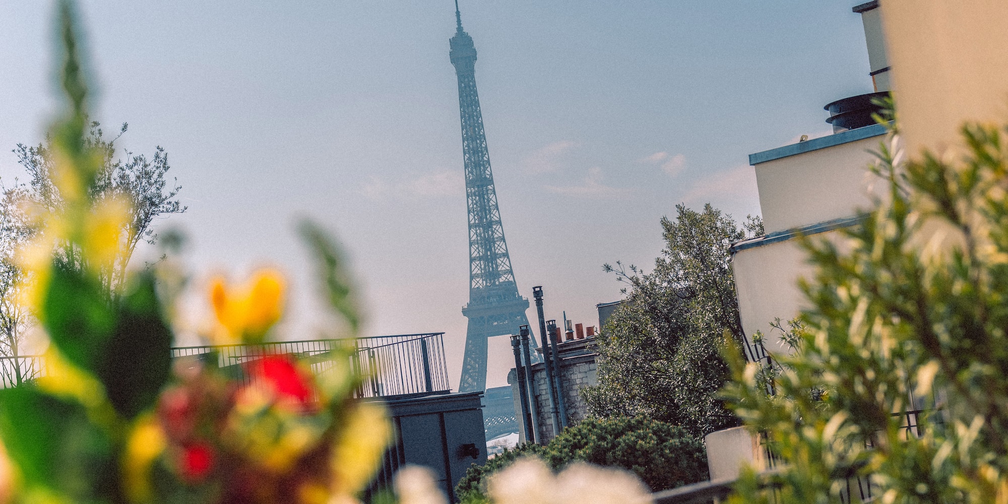 Eiffel Tower view from a Parisian balcony with blurred colorful flowers.