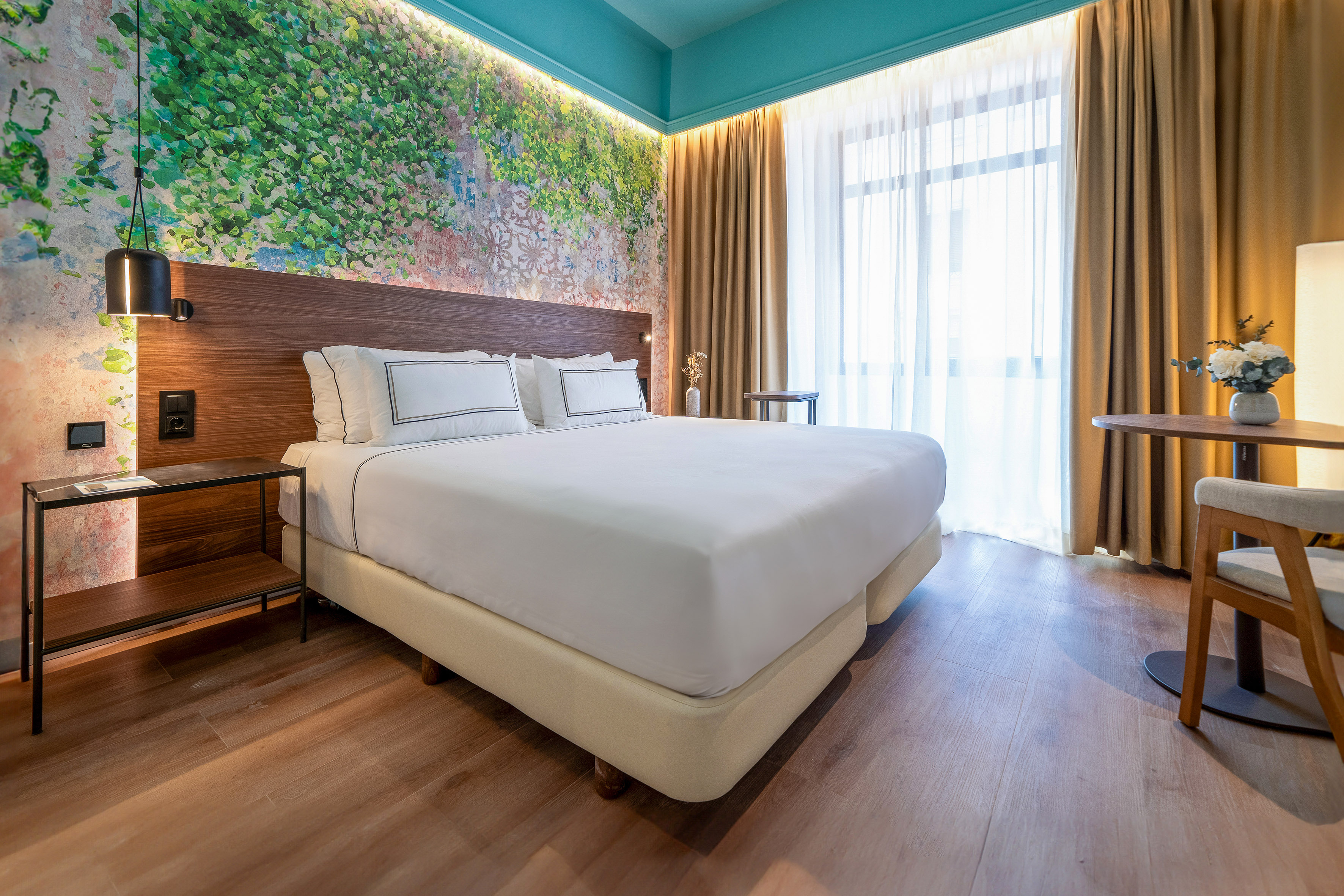 Modern hotel bedroom with king bed, green wall art, teal ceiling, wood floor.