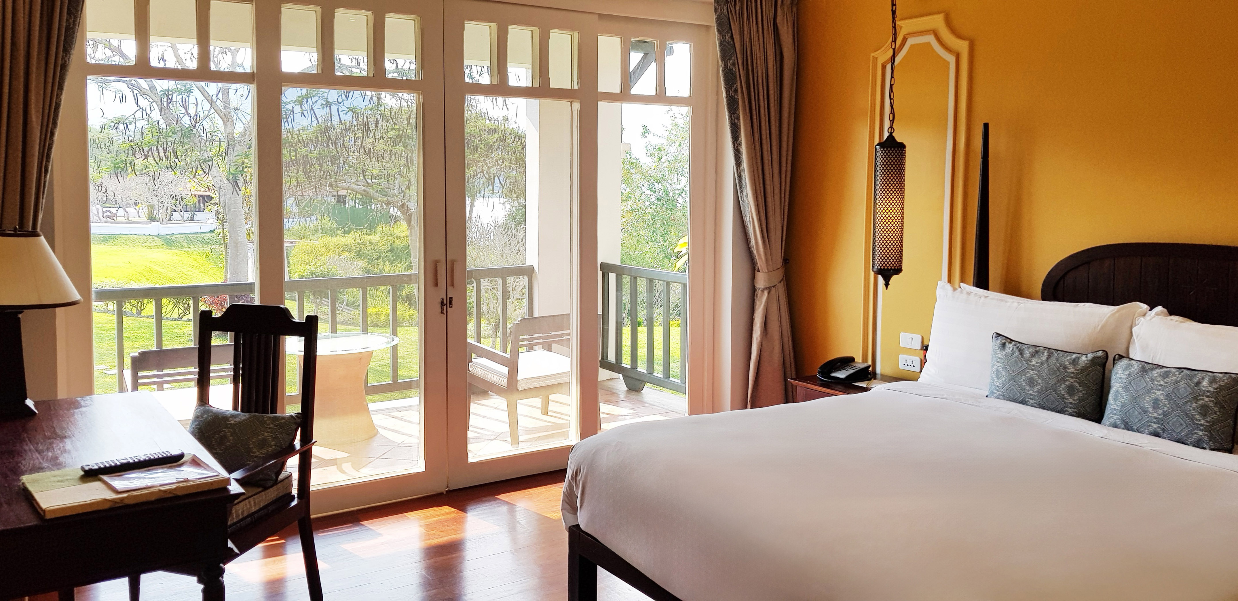 Resort bedroom with balcony overlooking a lush garden.