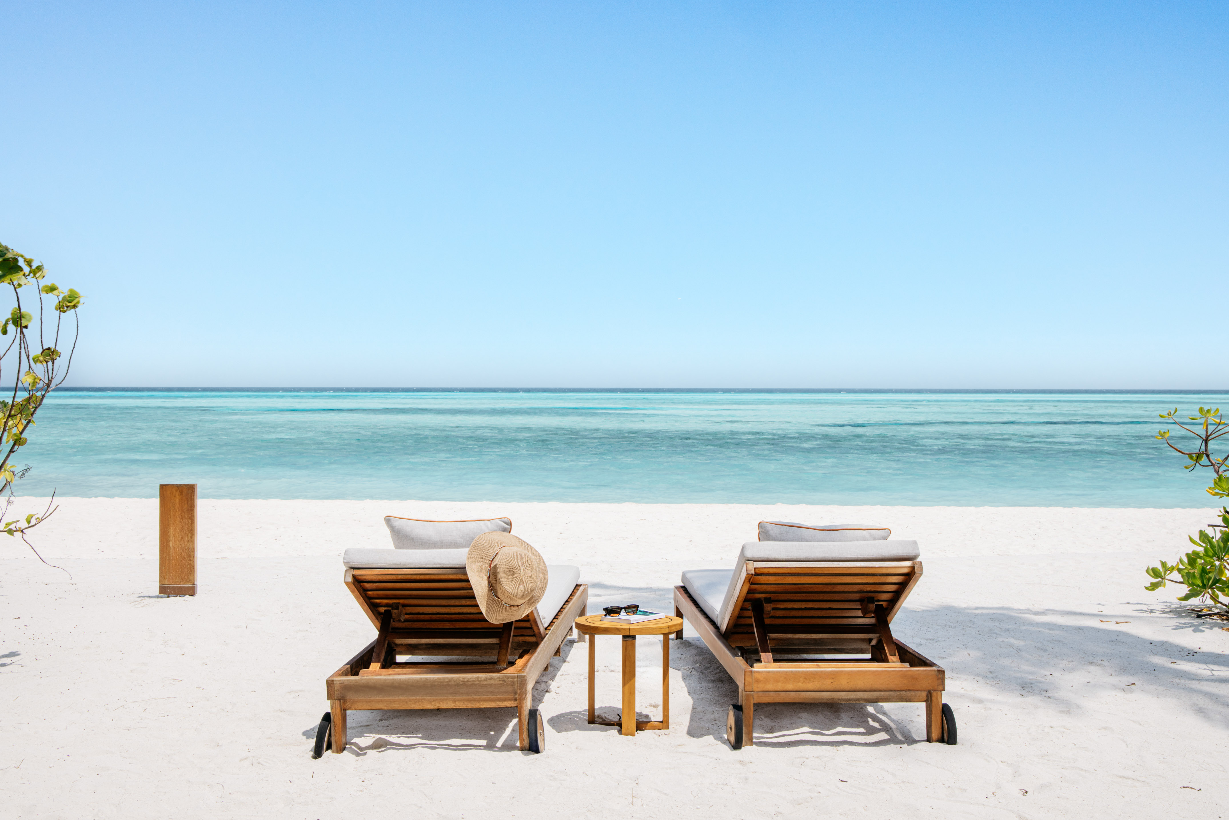Two wooden lounge chairs on white sand beach facing turquoise ocean.