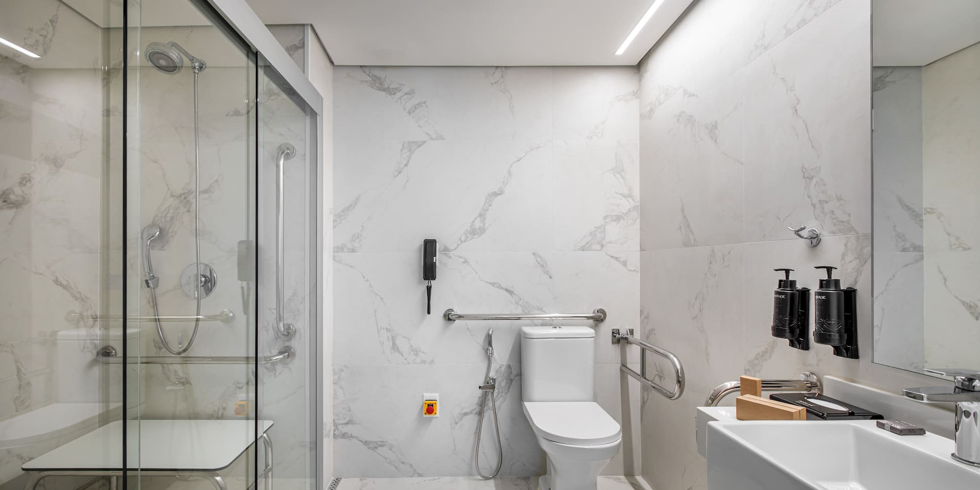 ADA compliant bathroom with roll-in shower, grab bars, seat, and marble finish.