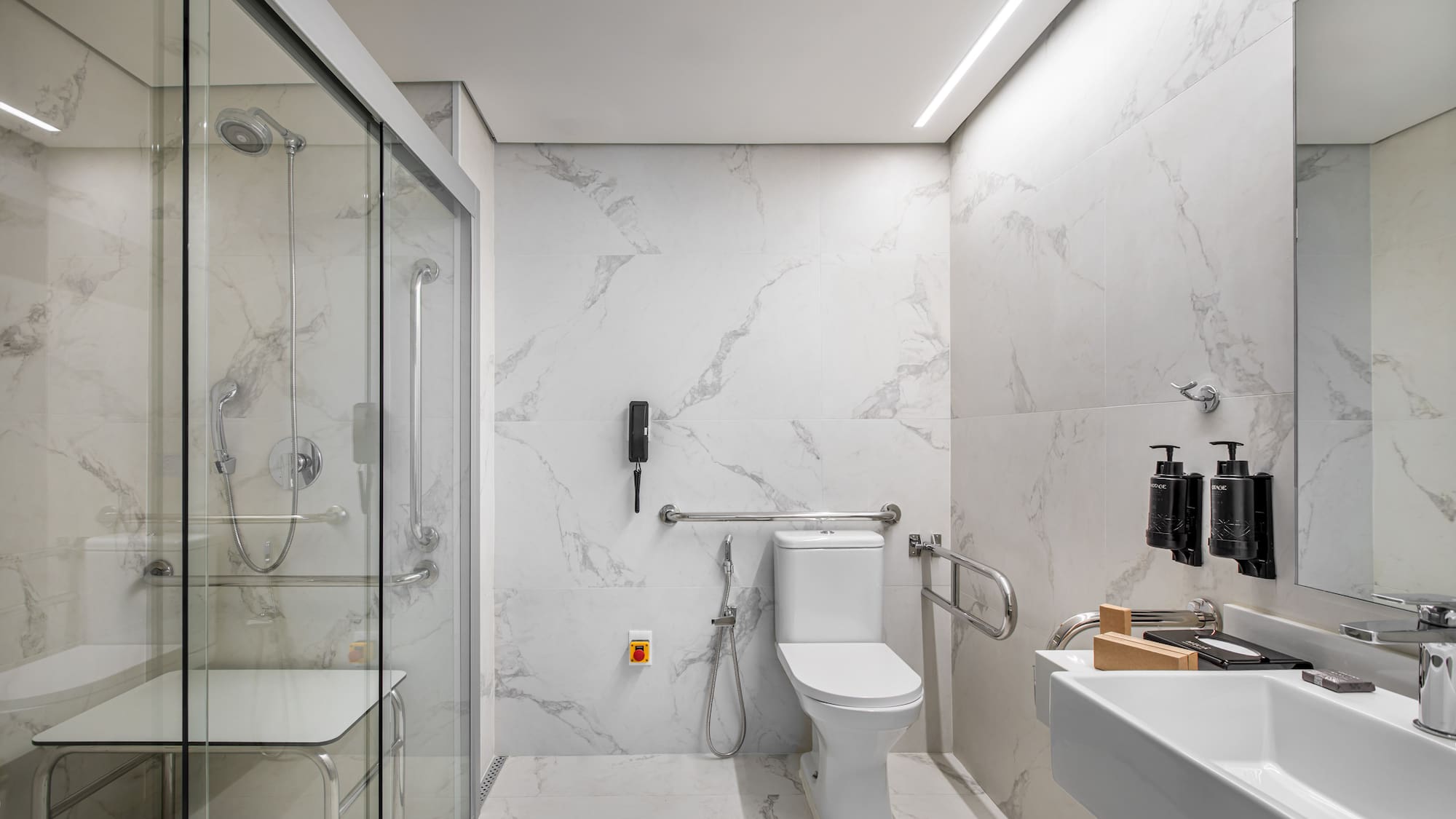 ADA compliant bathroom with roll-in shower, grab bars, seat, and marble finish.