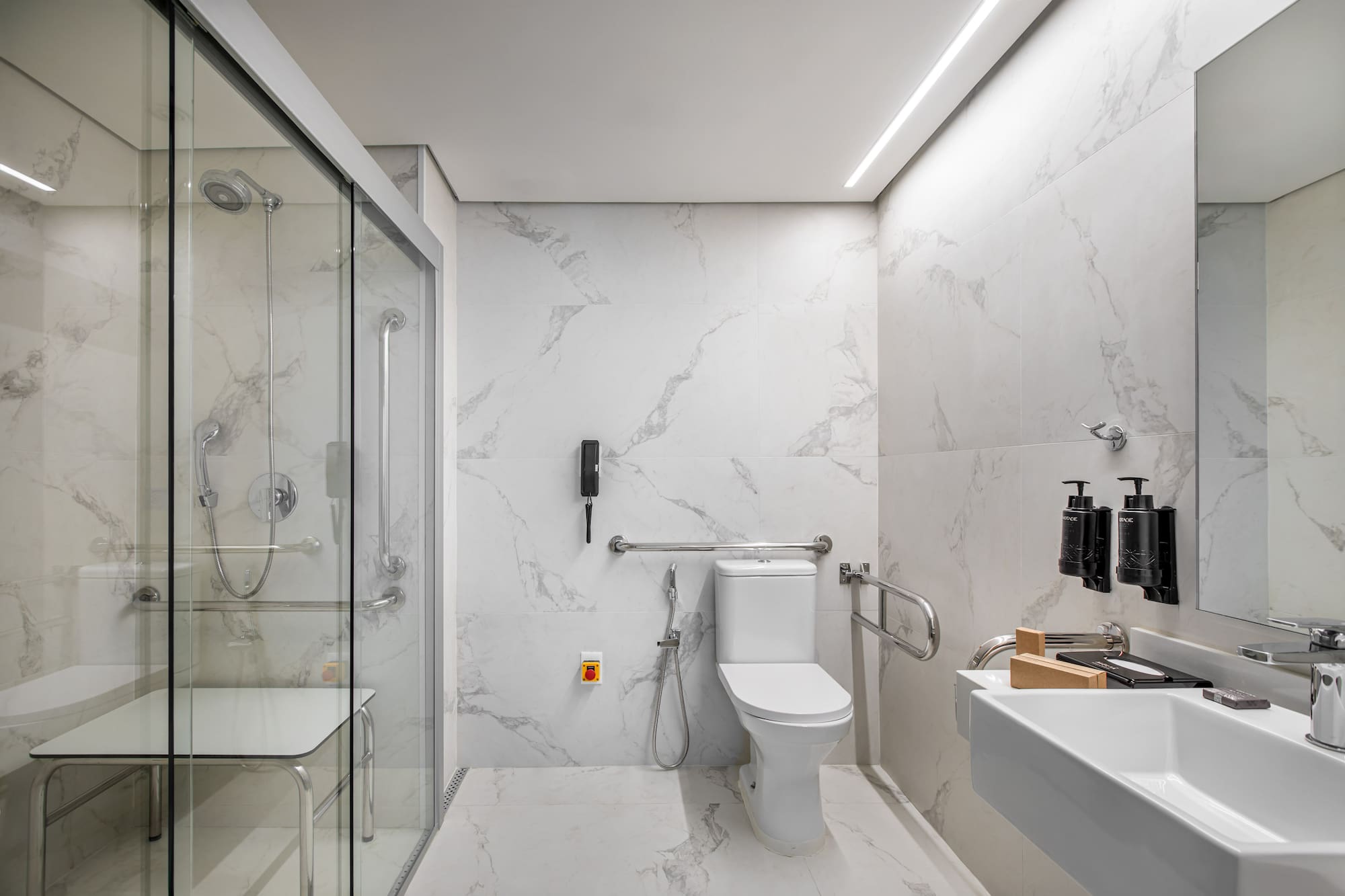 ADA compliant bathroom with roll-in shower, grab bars, seat, and marble finish.