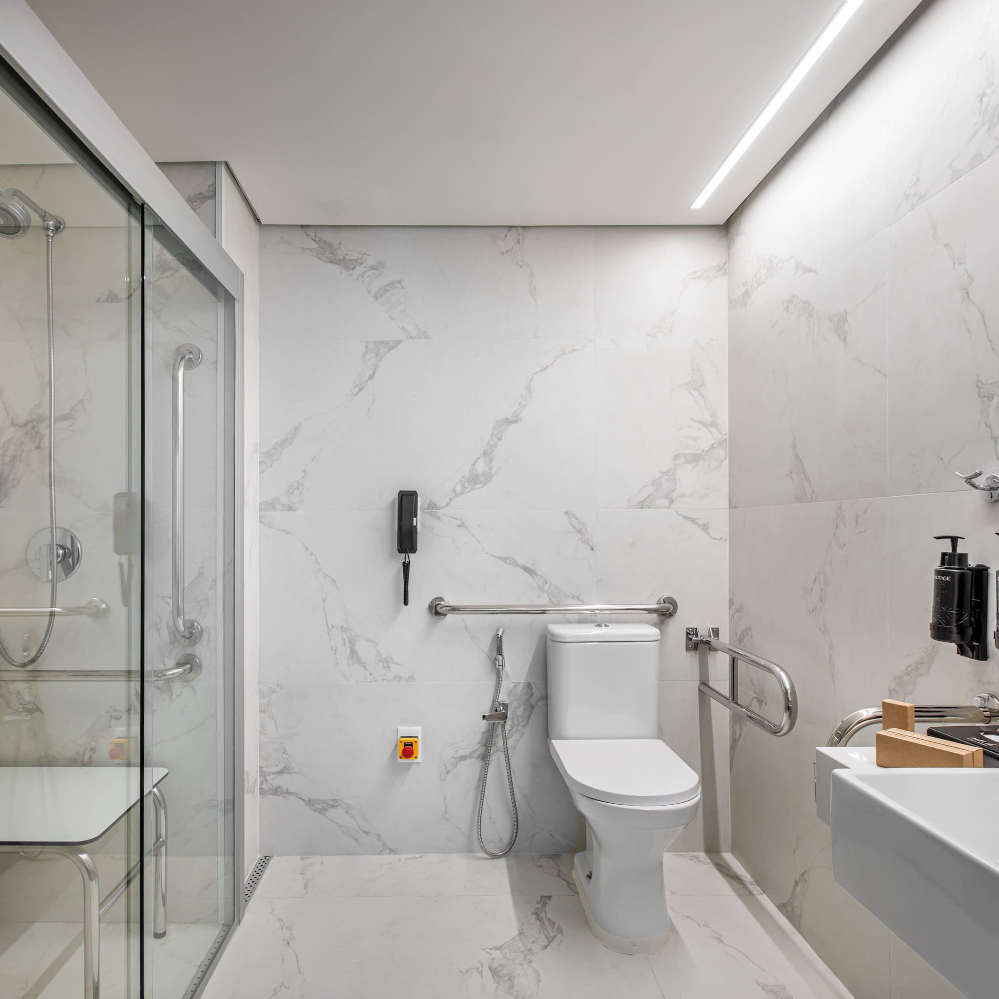 ADA compliant bathroom with roll-in shower, grab bars, seat, and marble finish.