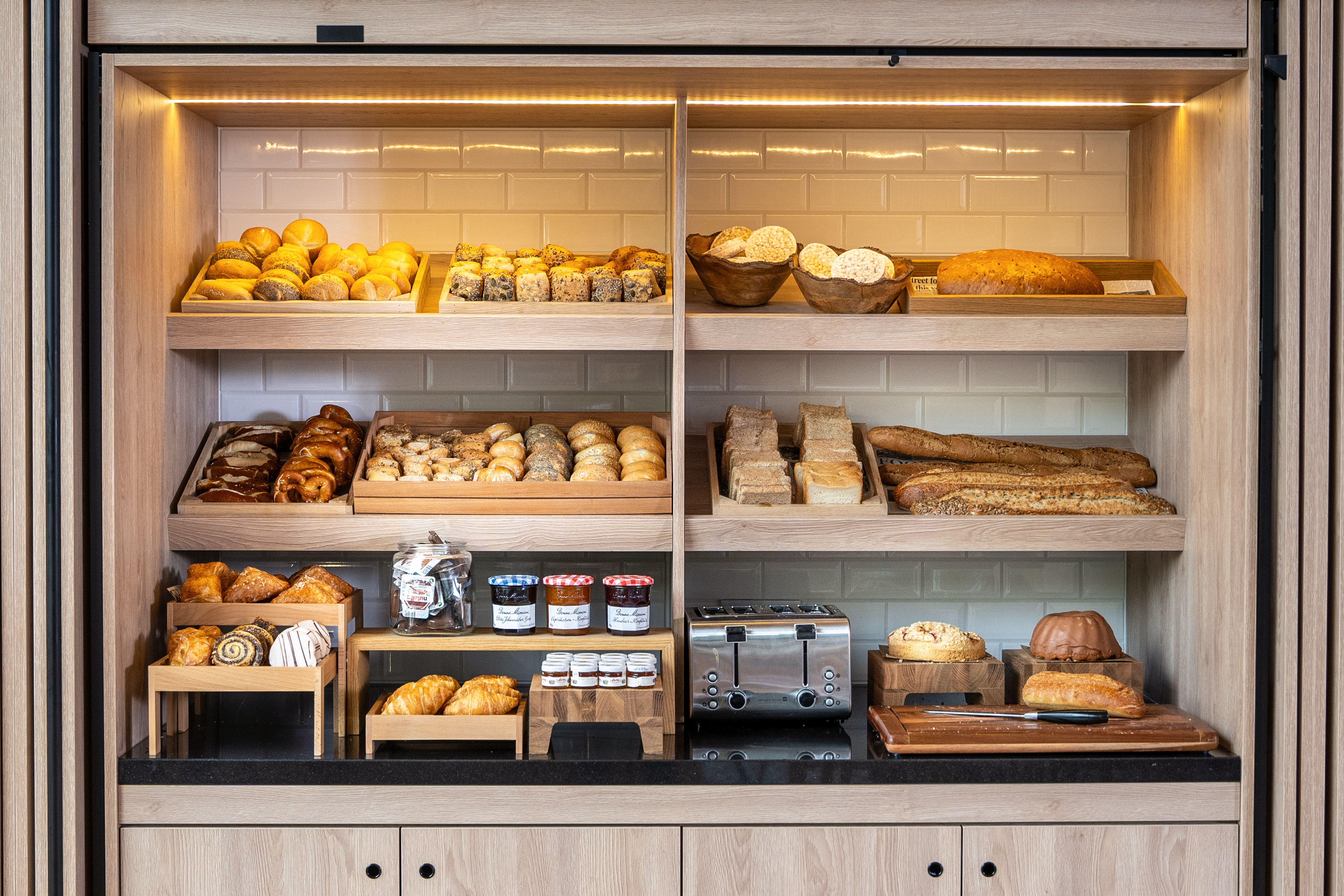 Breakfast buffet display with assorted breads, pastries, jams, and toaster.