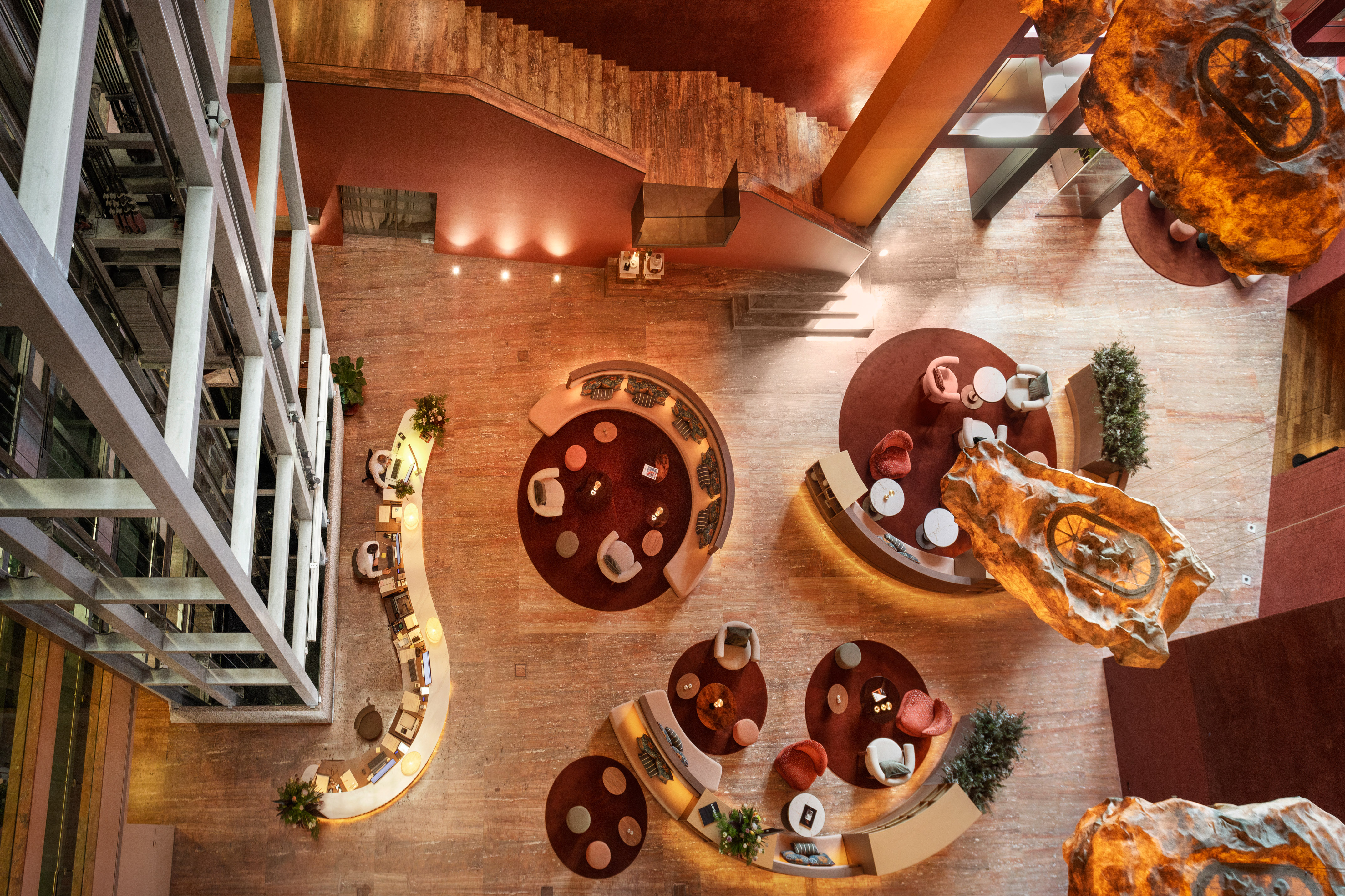 Modern hotel lobby with curved lounge seating, grand staircase, and organic light sculptures.