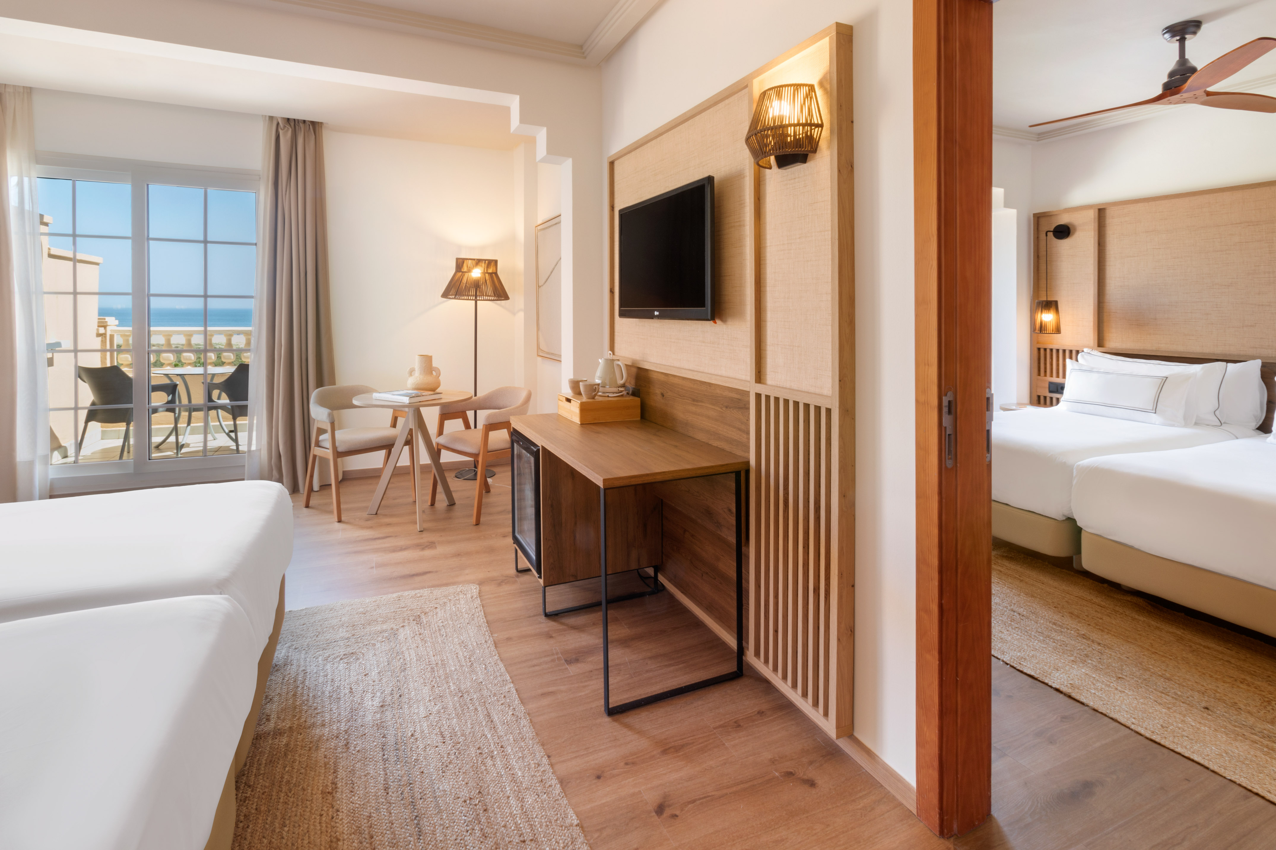 Coastal hotel room with ocean view balcony, twin beds, natural wood design.