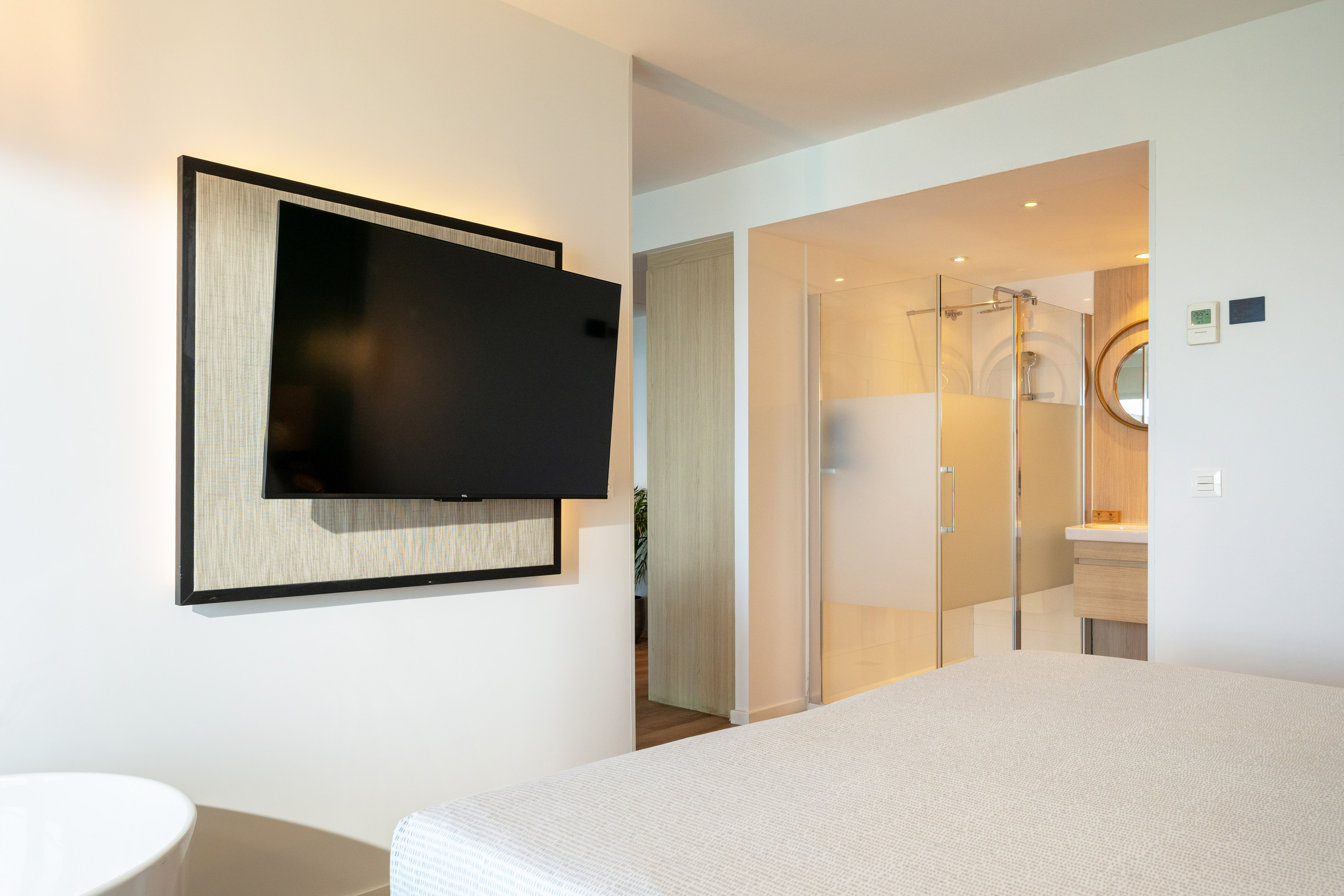 Modern hotel bedroom with wall-mounted TV, bed, and open ensuite bathroom.