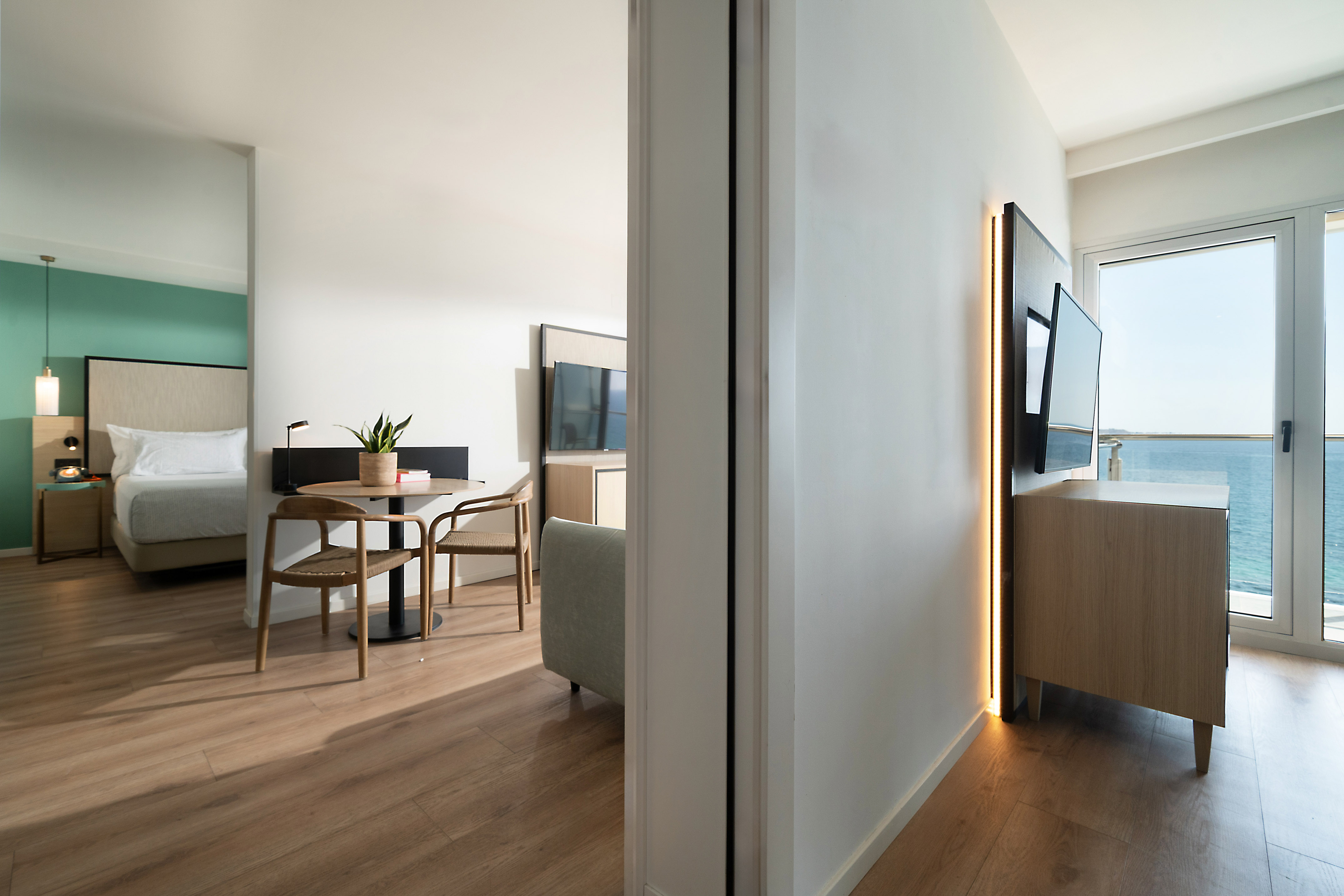 Modern hotel suite with ocean view, bedroom, dining area, and balcony.