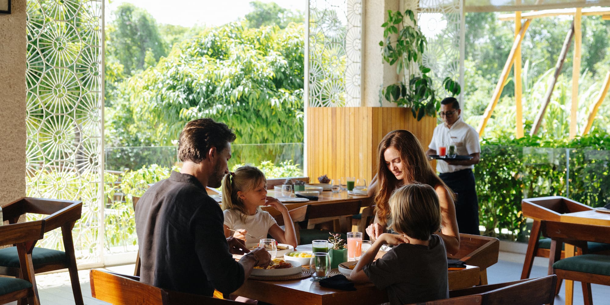Family dining at a tropical resort restaurant with lush green views.