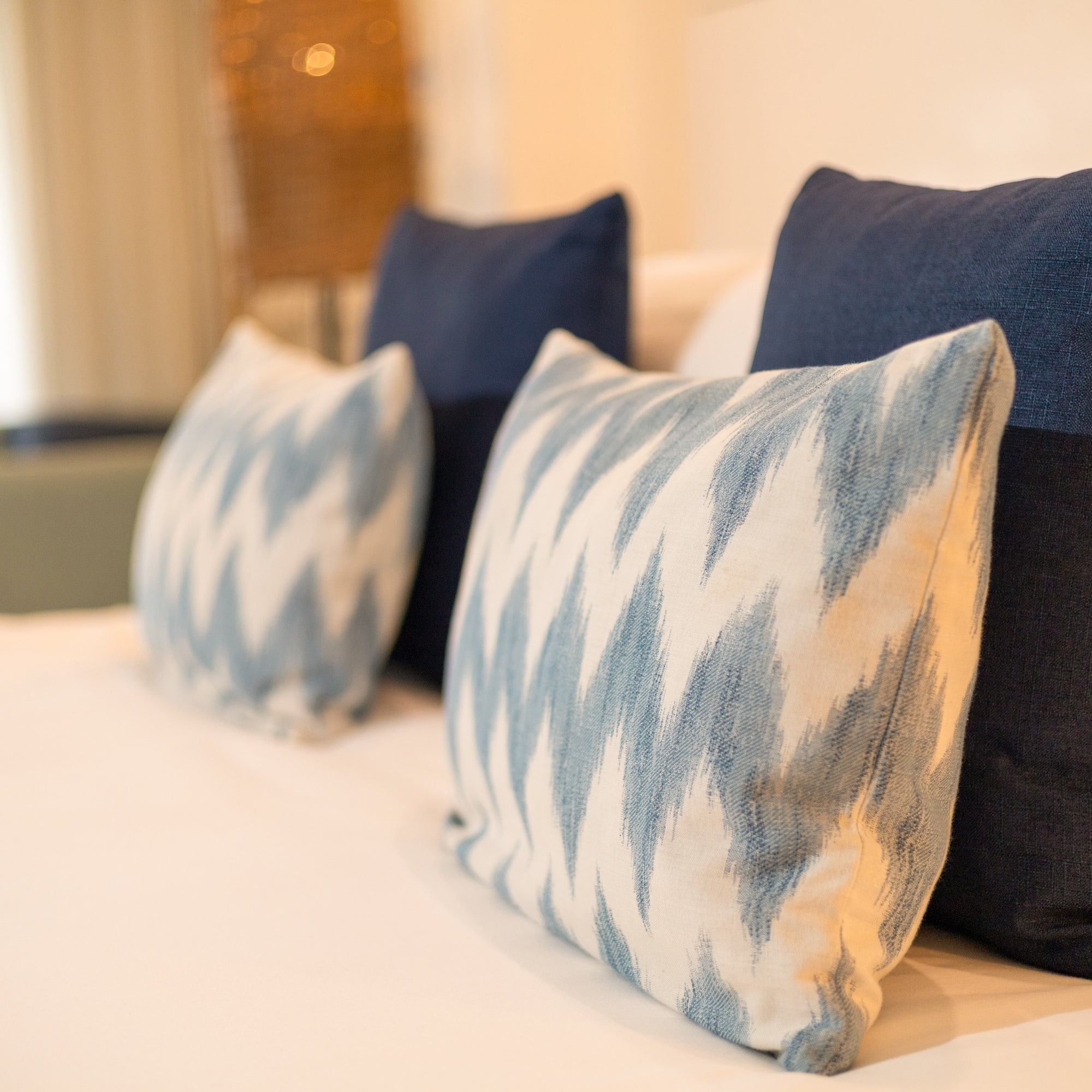 Blue and white decorative bed pillows with ikat pattern on a hotel bed.