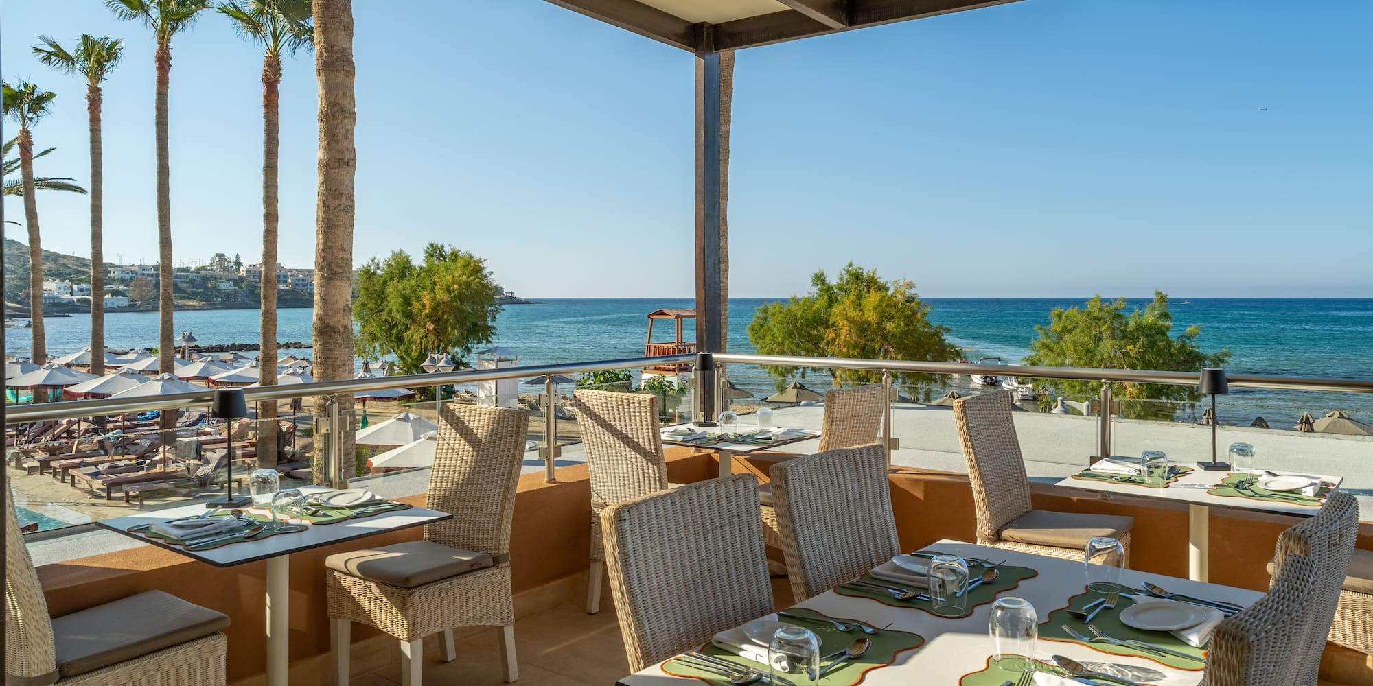 Resort restaurant balcony with ocean view, set tables, and tropical palm trees.