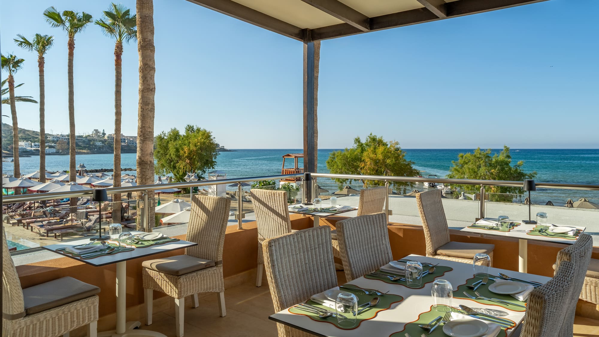 Resort restaurant balcony with ocean view, set tables, and tropical palm trees.