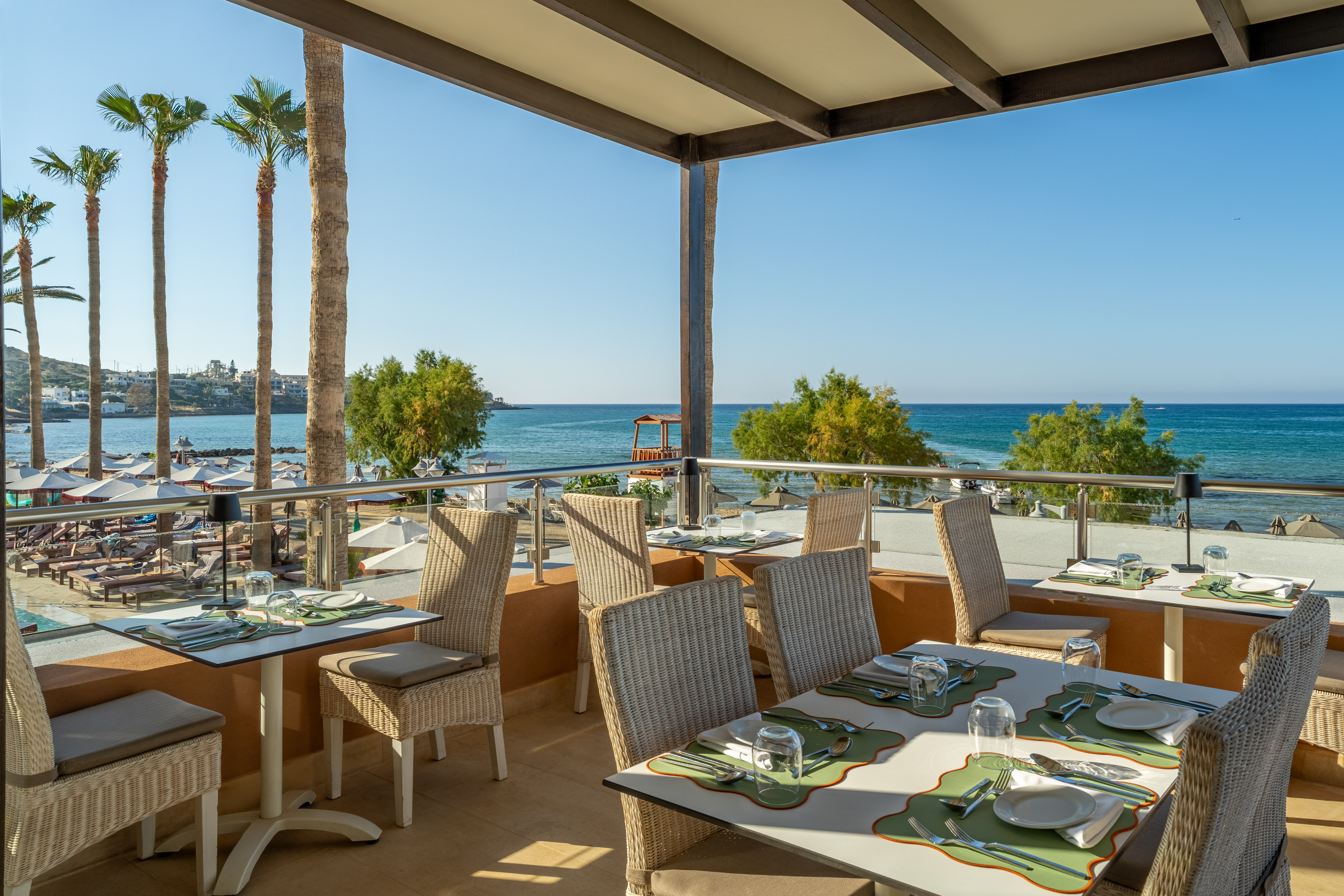 Resort restaurant balcony with ocean view, set tables, and tropical palm trees.