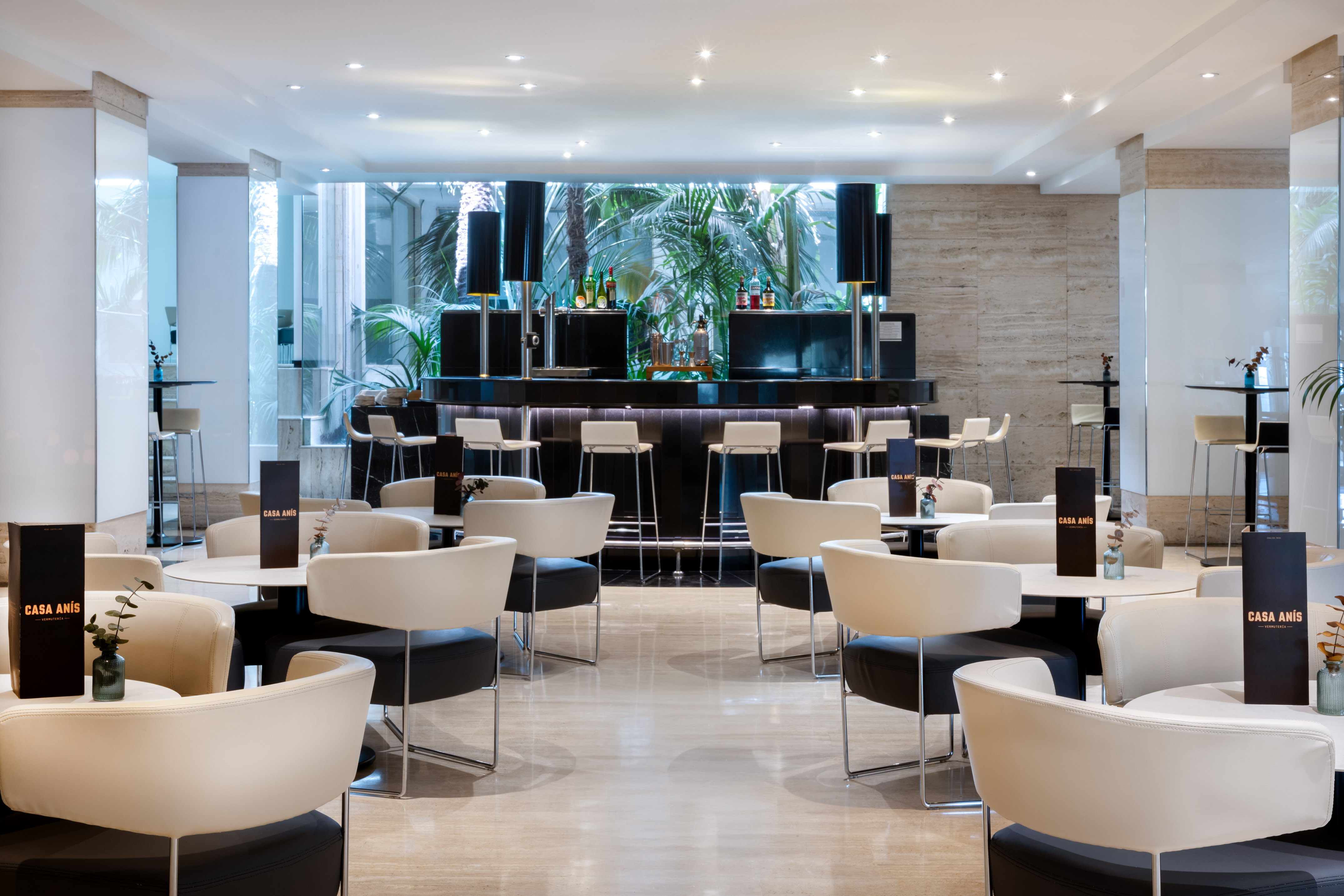 Stylish Casa Anís bar lounge, cream seating, black counter, tropical garden view.