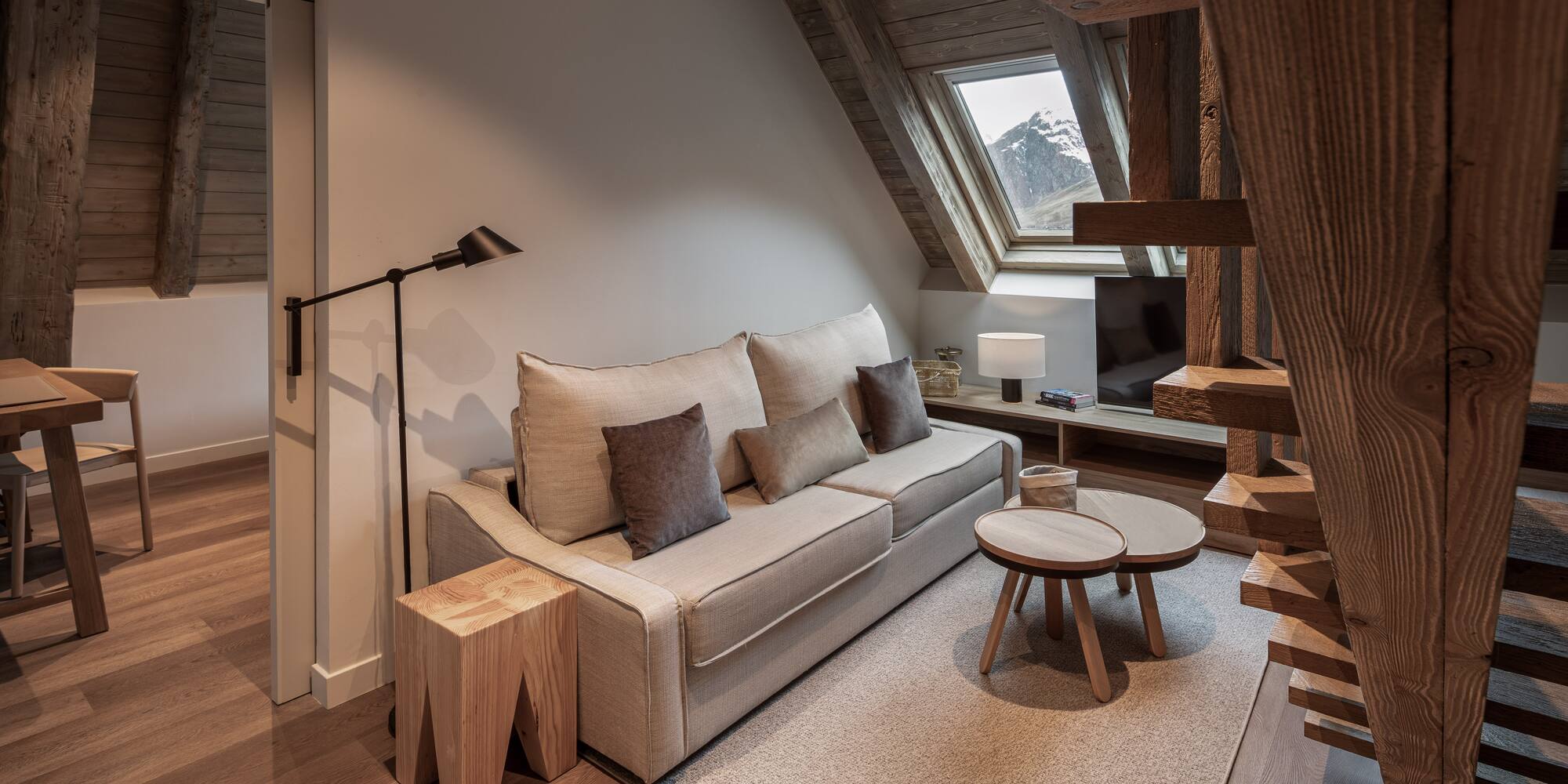 Cozy living room, sofa, wooden beams, and mountain view from attic window.